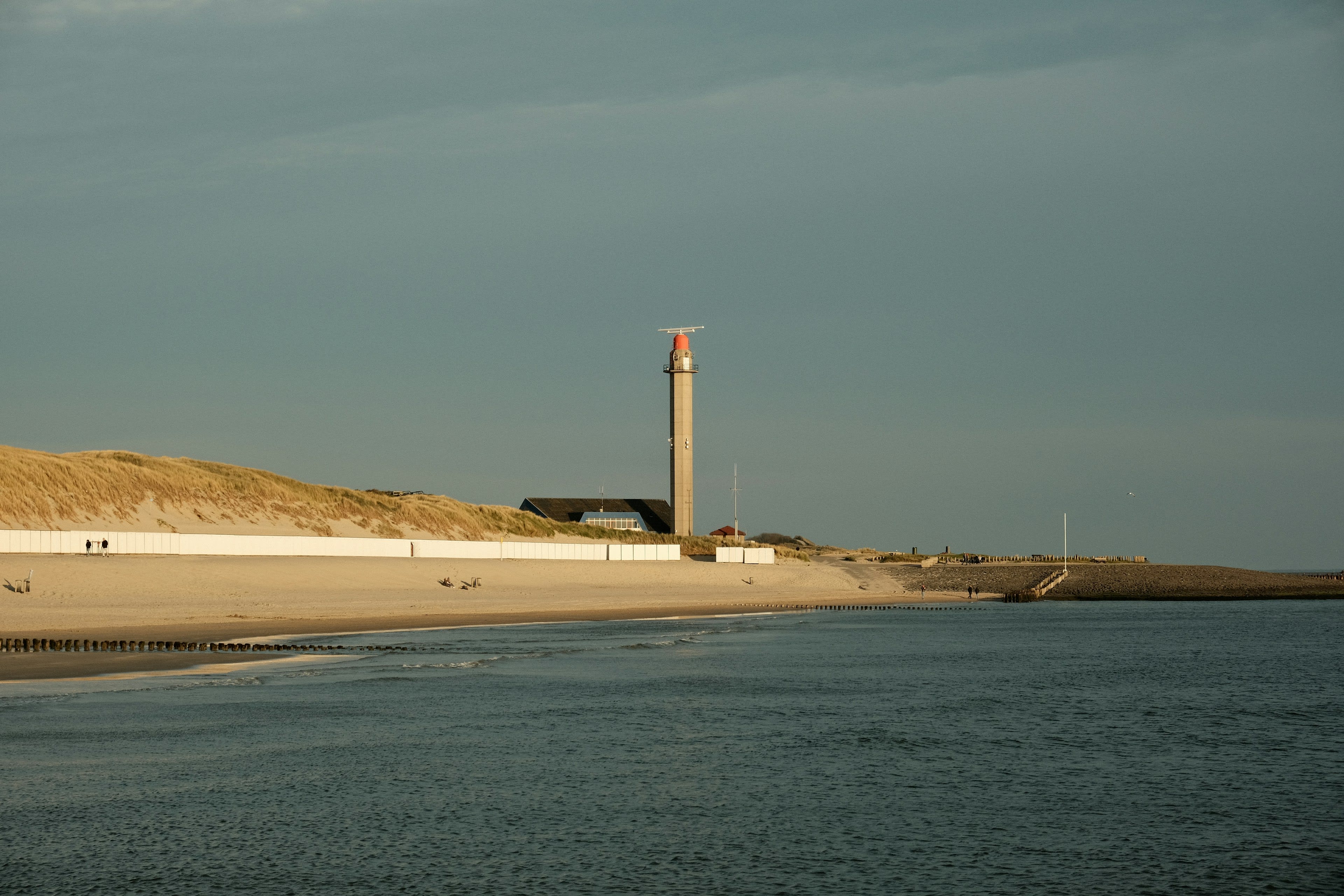Sand dunes and a lighthouse along a grey-blue North Sea shore