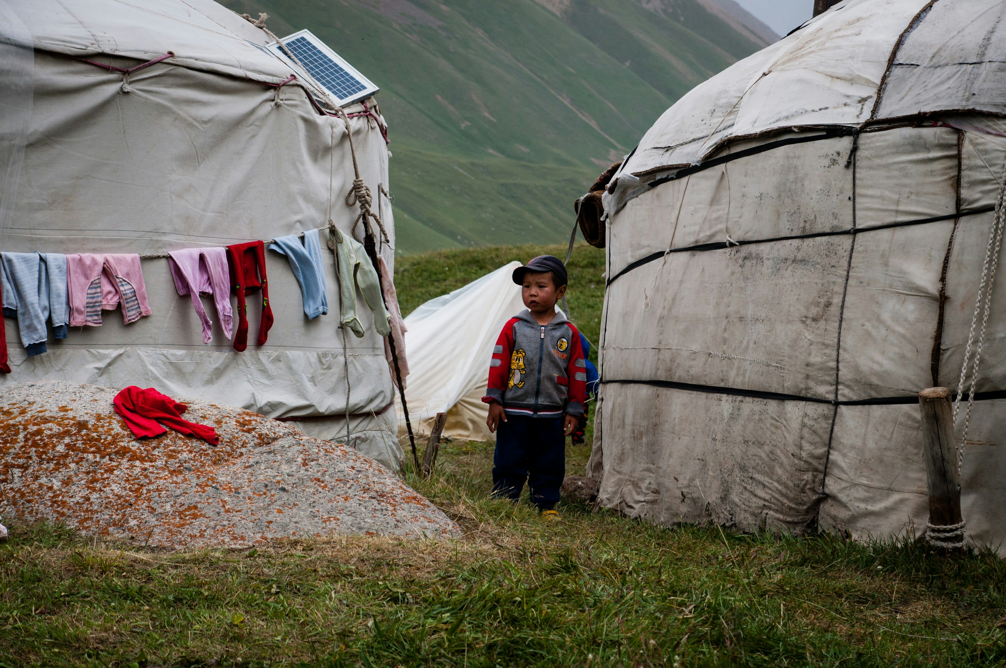 Children's washing pegged on a line beside a felt yurt with a child standing by the door