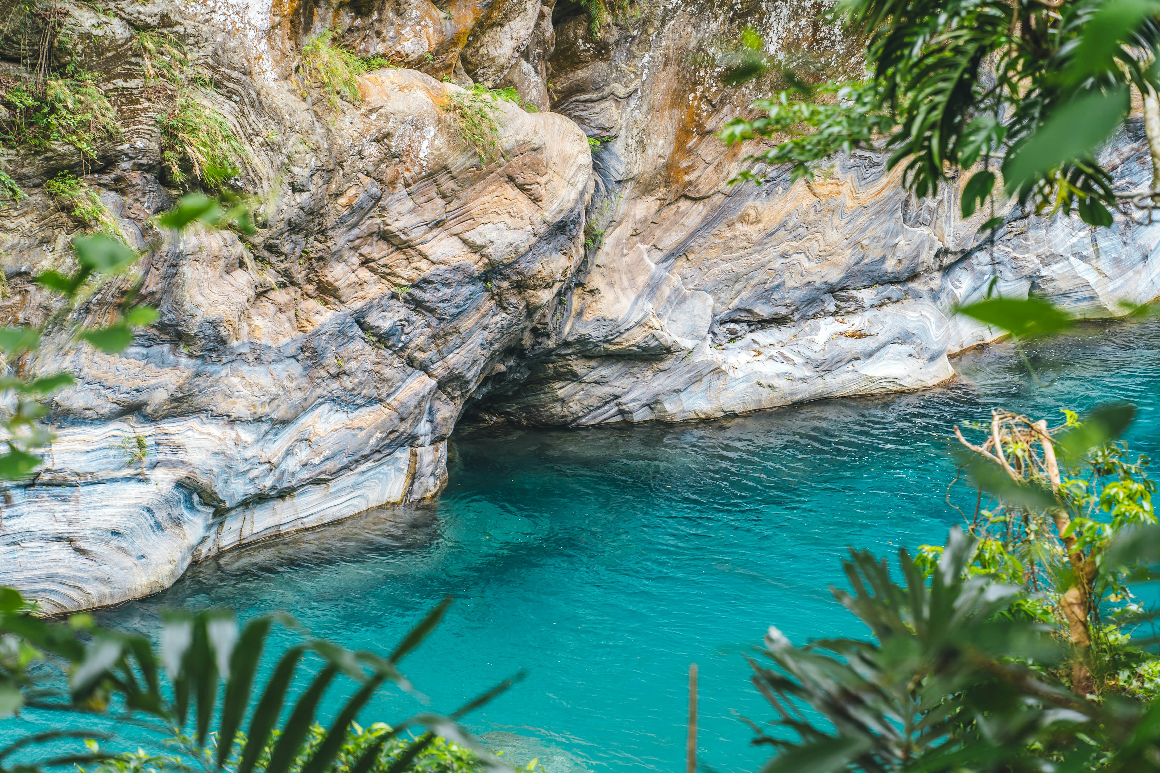 Bright turquoise water in a narrow marble channel overhung with ferns