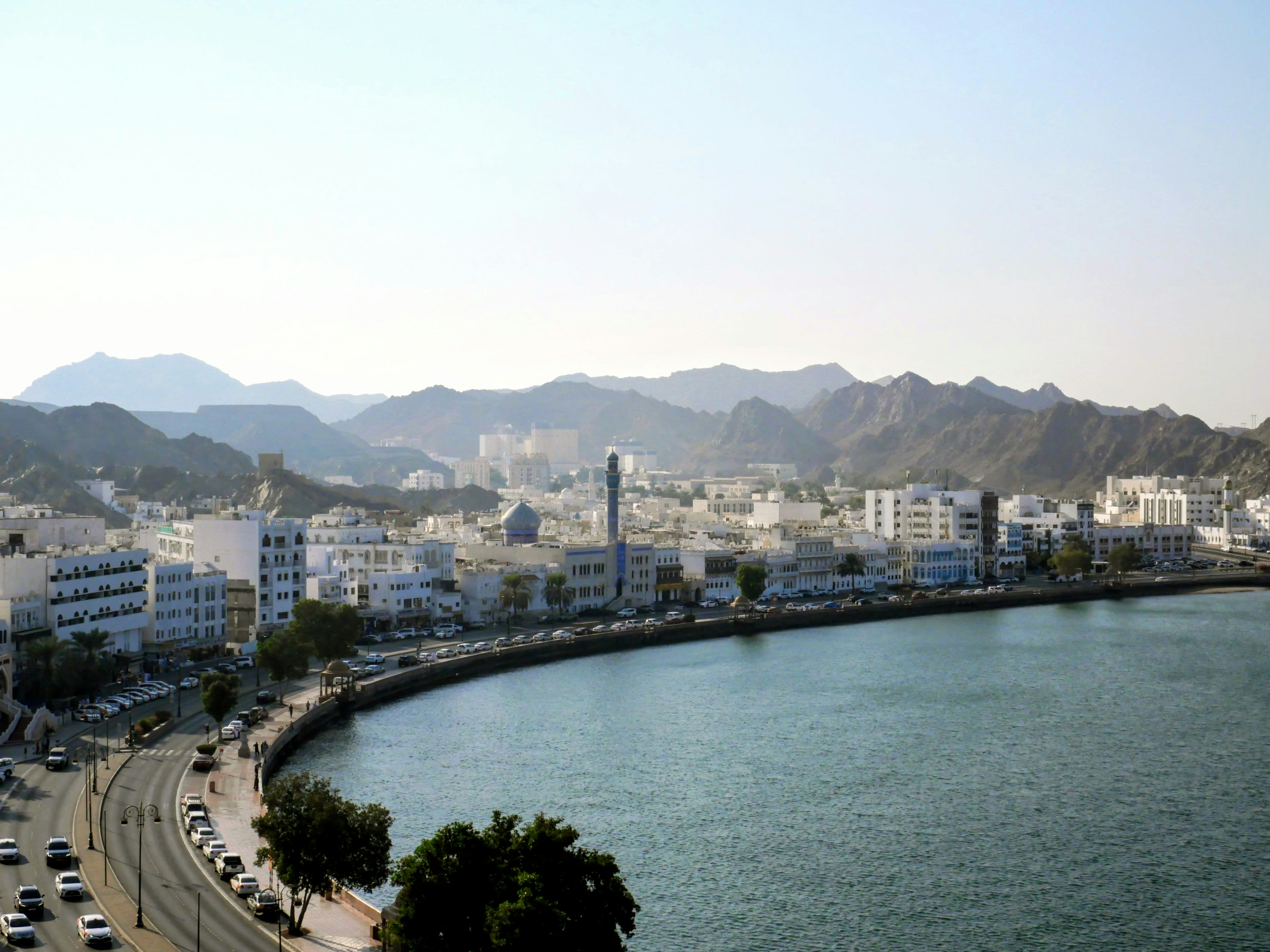 White low-rise city curving around a bay beneath dark rocky mountains