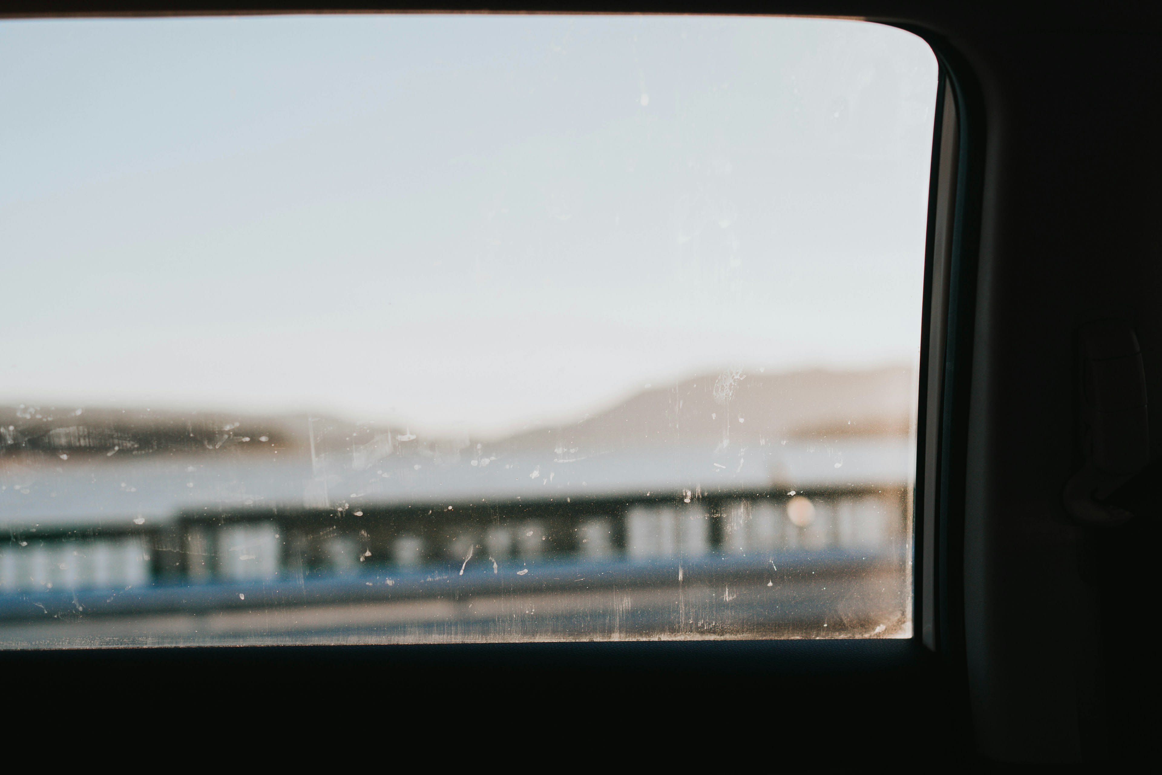 Rain running down a car window with grey water and a low shoreline beyond