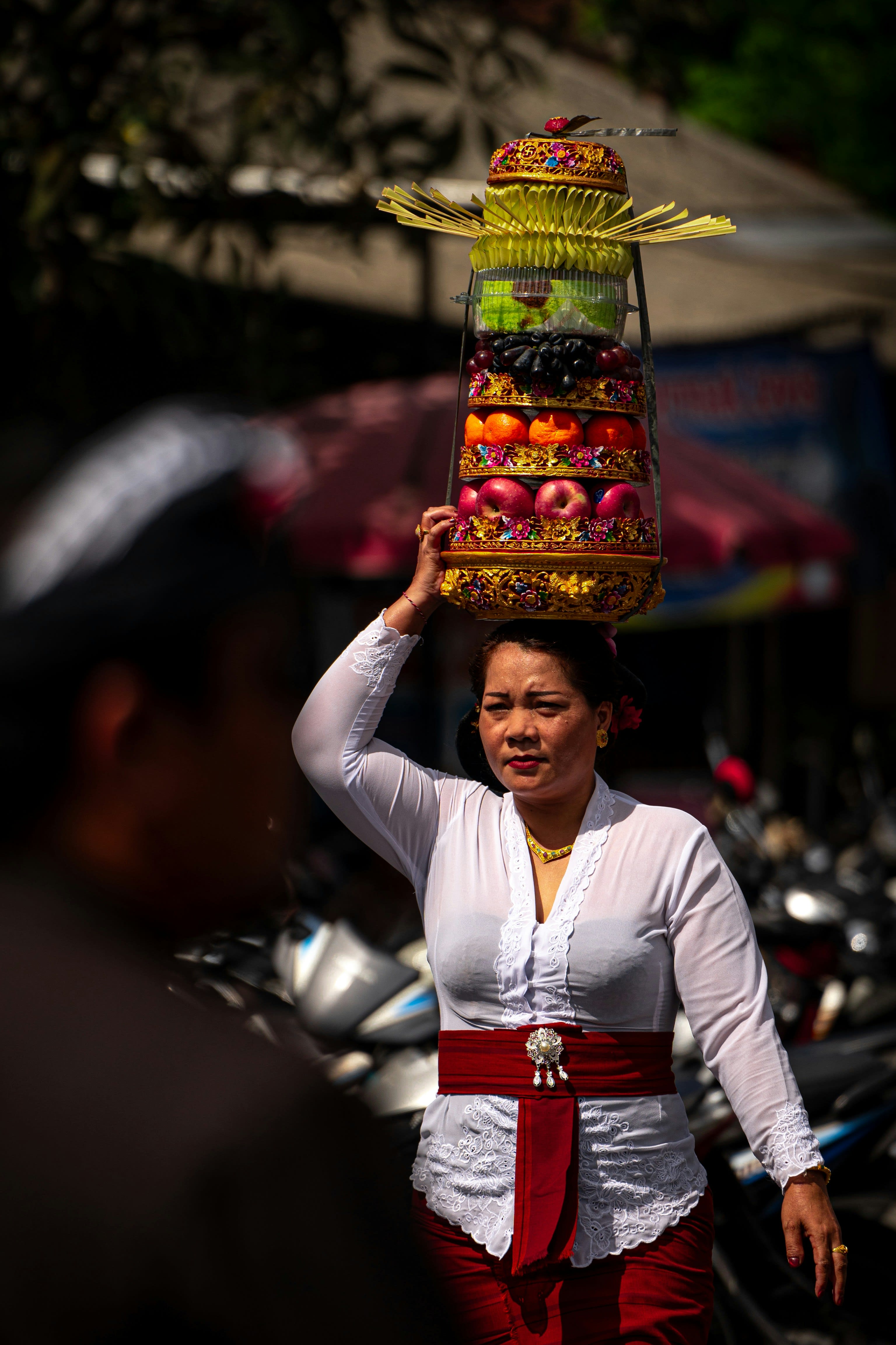 A woman carrying a tall tower of fruit offerings on her head