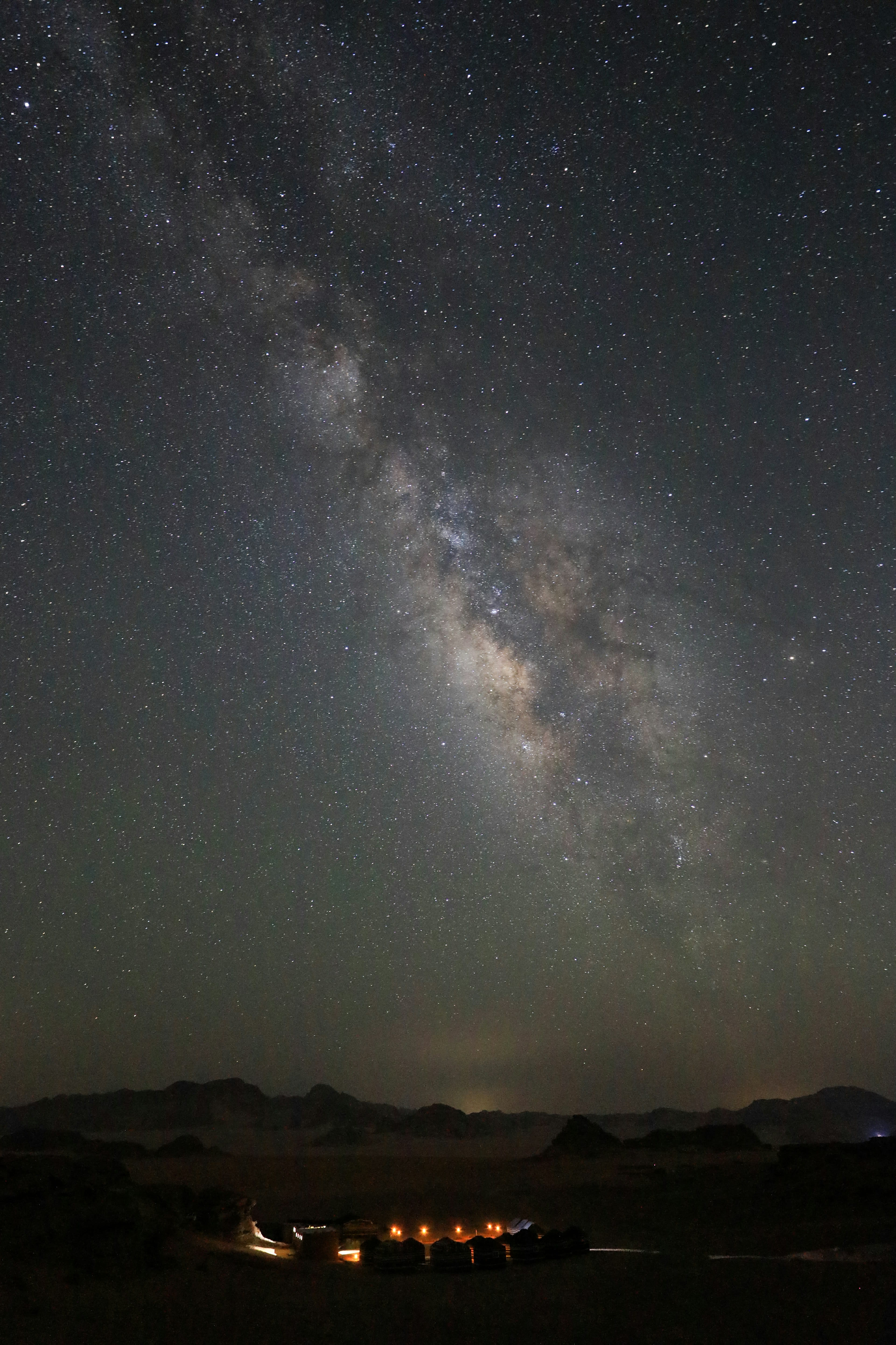 The Milky Way over a dark desert with a low lit shelter in the foreground