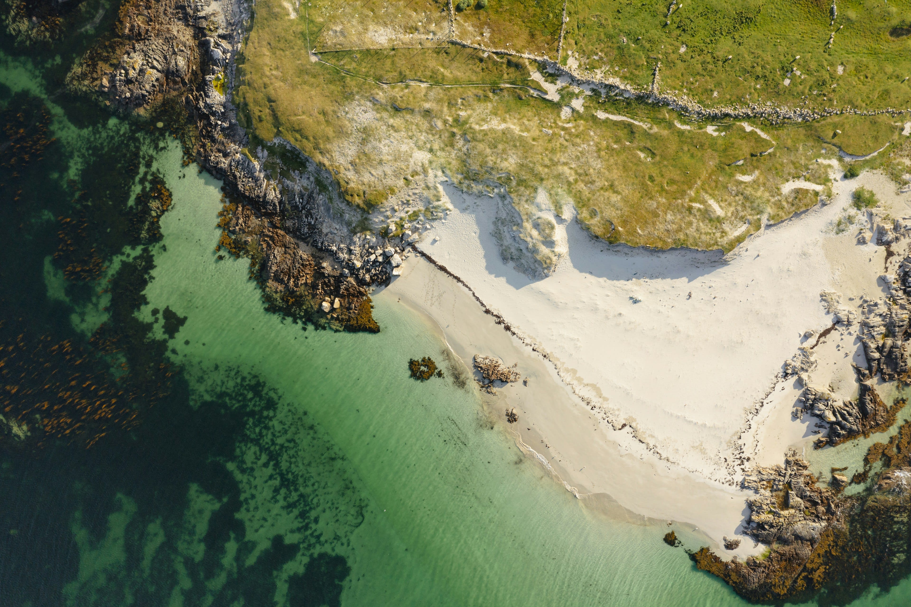 Aerial view of a white sand cove with turquoise water and green headland