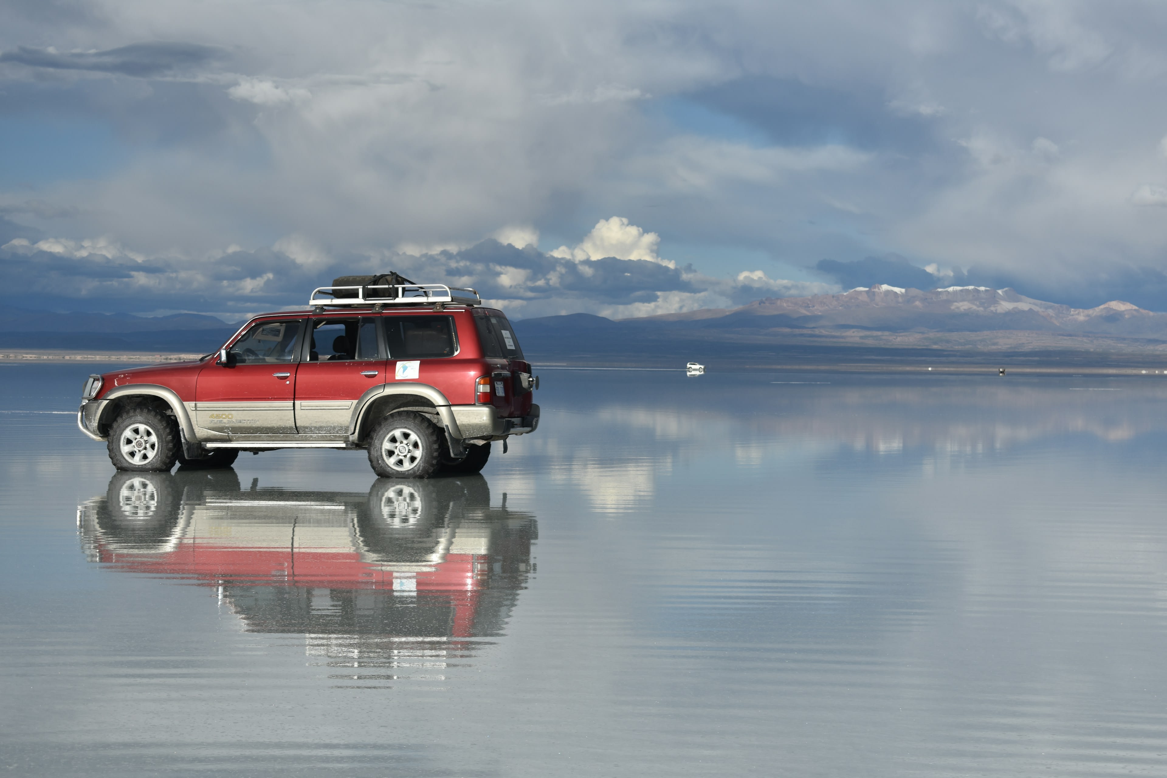 A red 4x4 reflected perfectly in shallow water on a salt flat