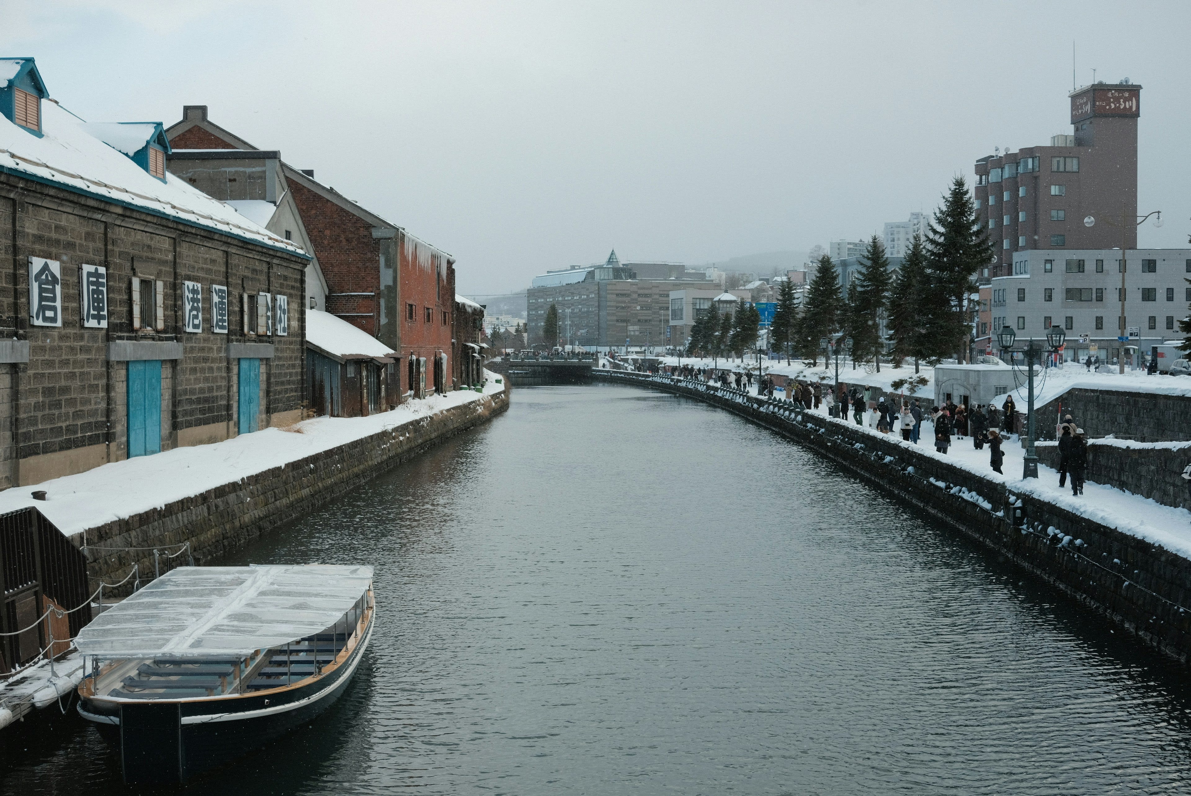 A small boat on the snow-edged Otaru canal beside old stone warehouses