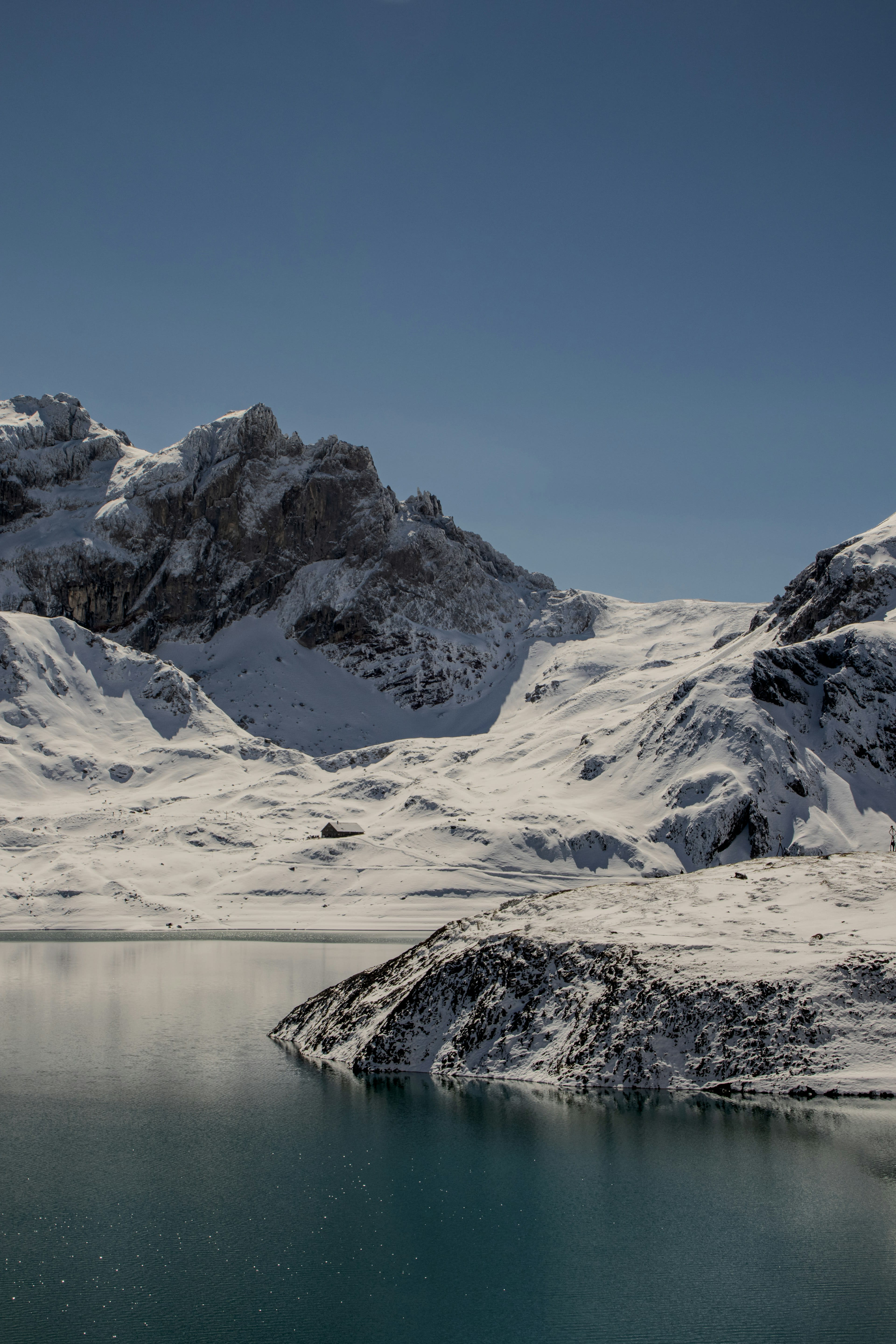 A pale glacial lake beneath bare snow-dusted peaks under flat cloud