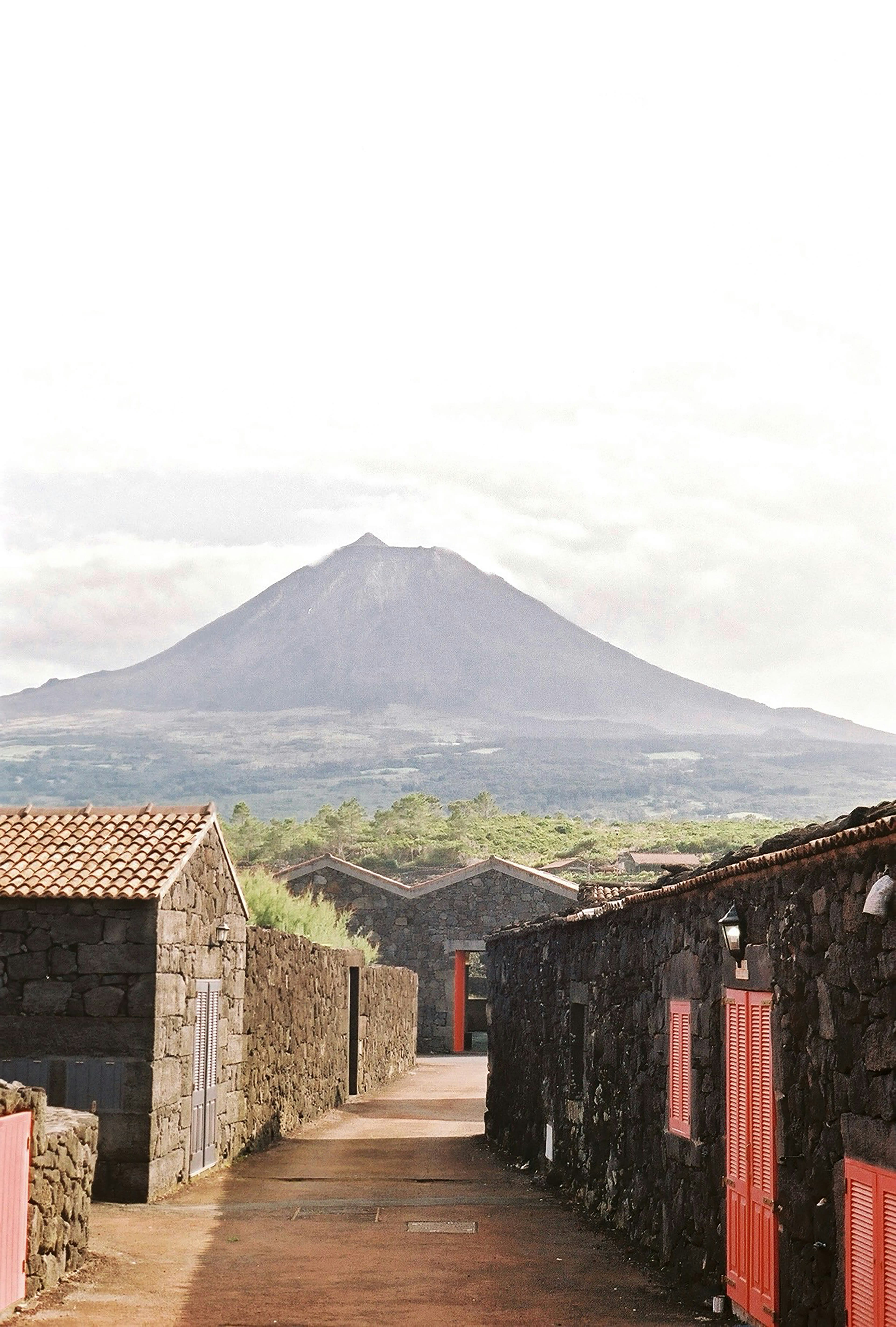 A stone lane between black basalt walls and buildings with a volcano rising behind