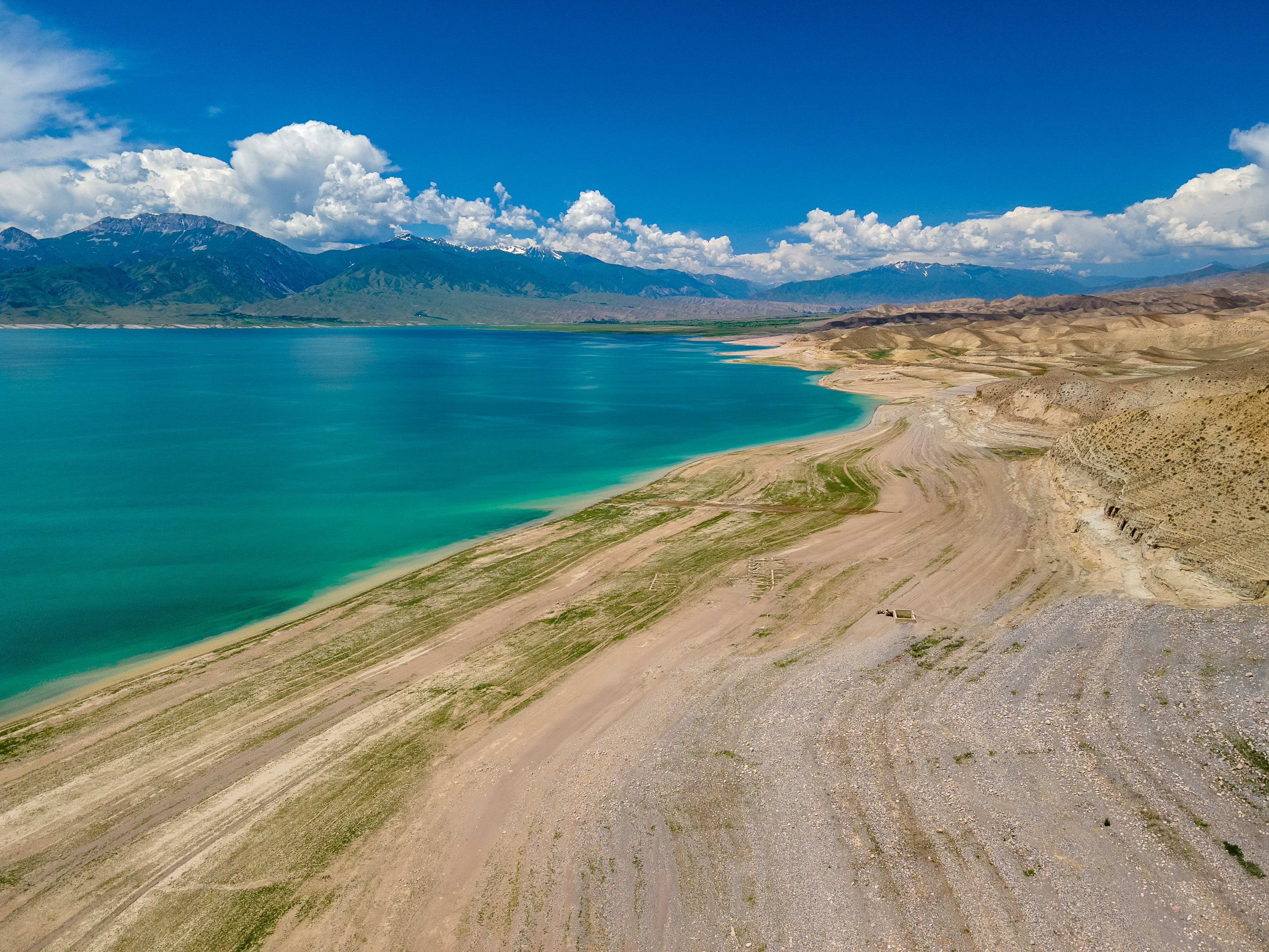A sandy track running down to a turquoise inland sea with a snow range on the far shore