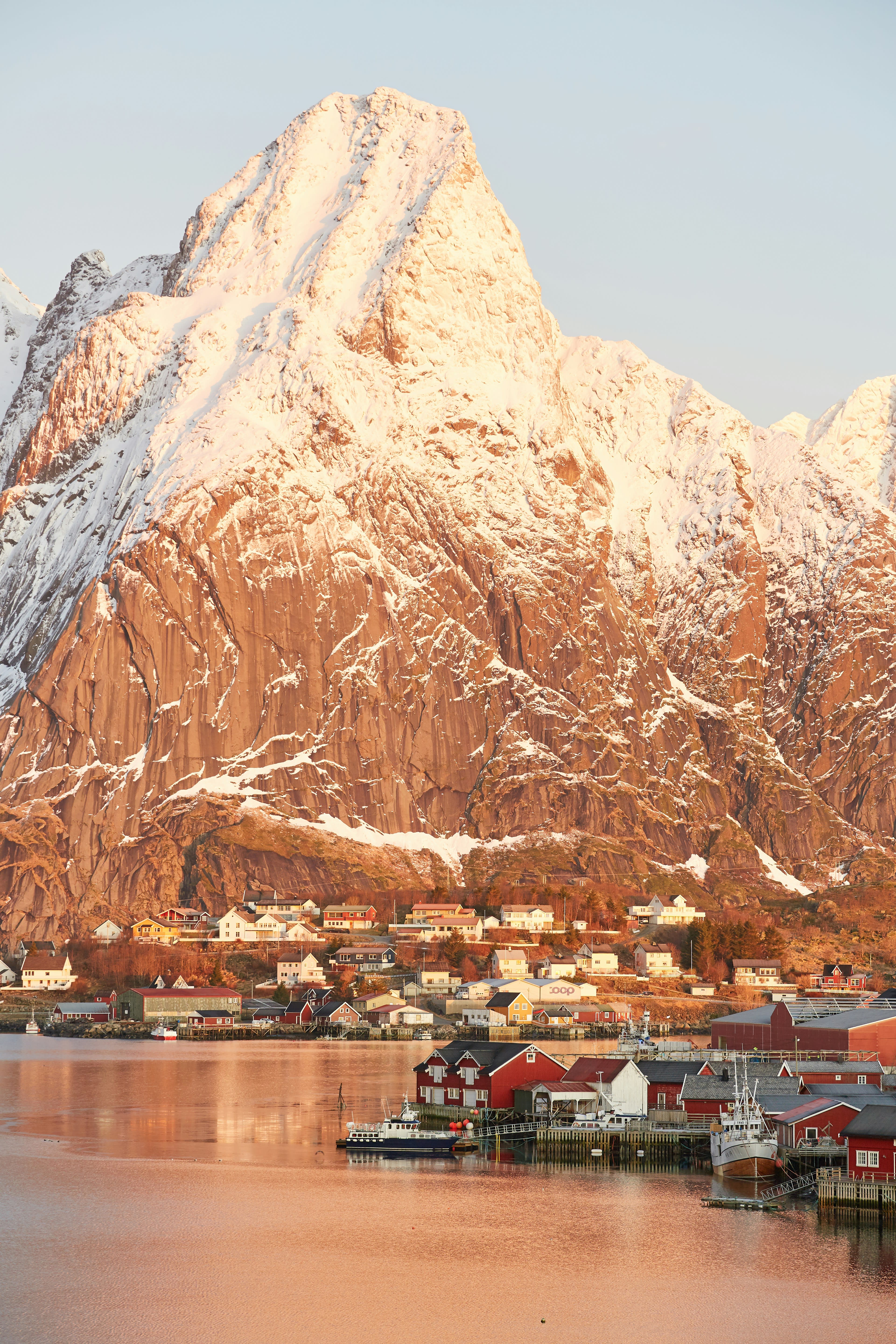 Pink dawn light on a snowy peak above a small harbour village