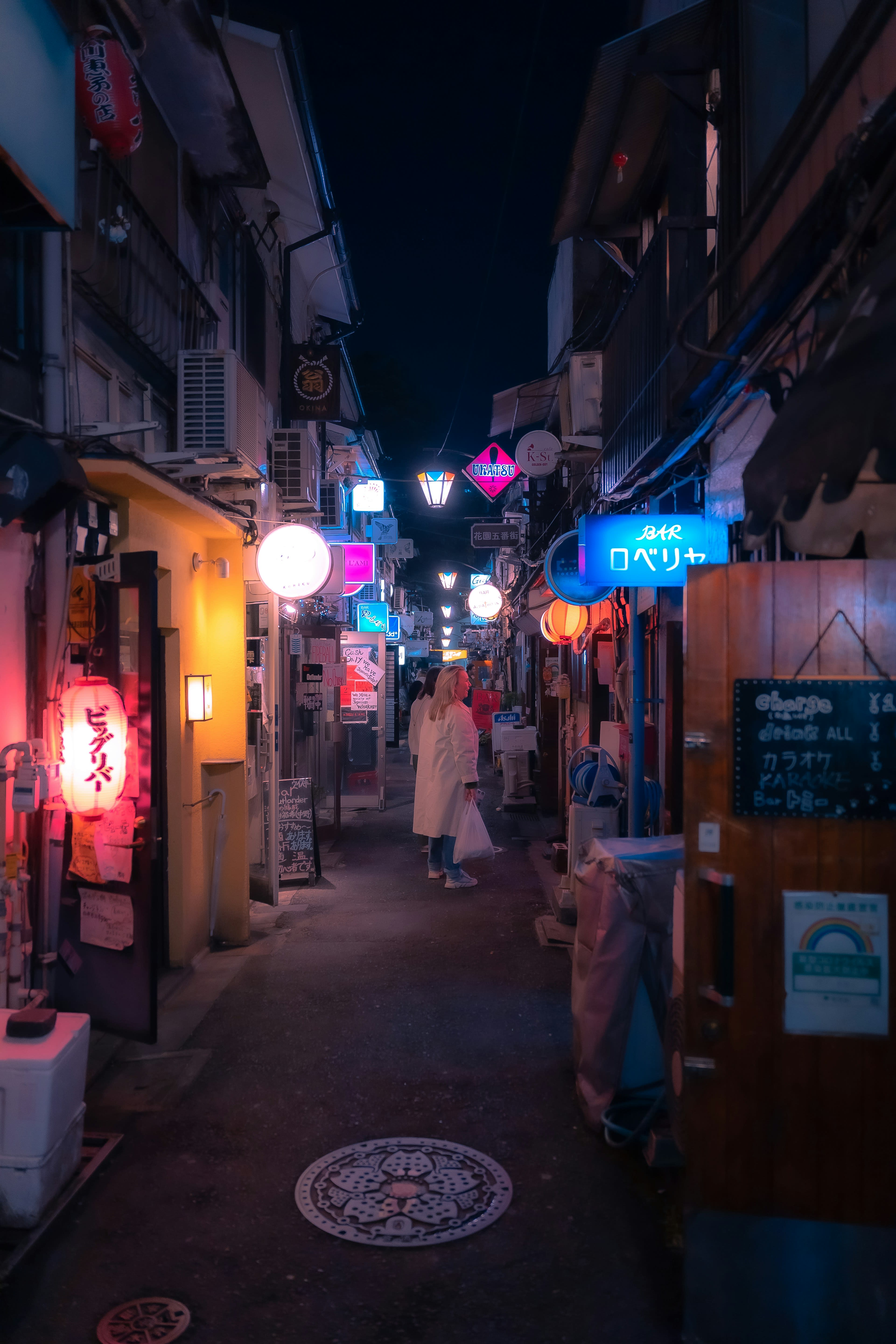 A person walking away down a narrow lantern-lit alley at night