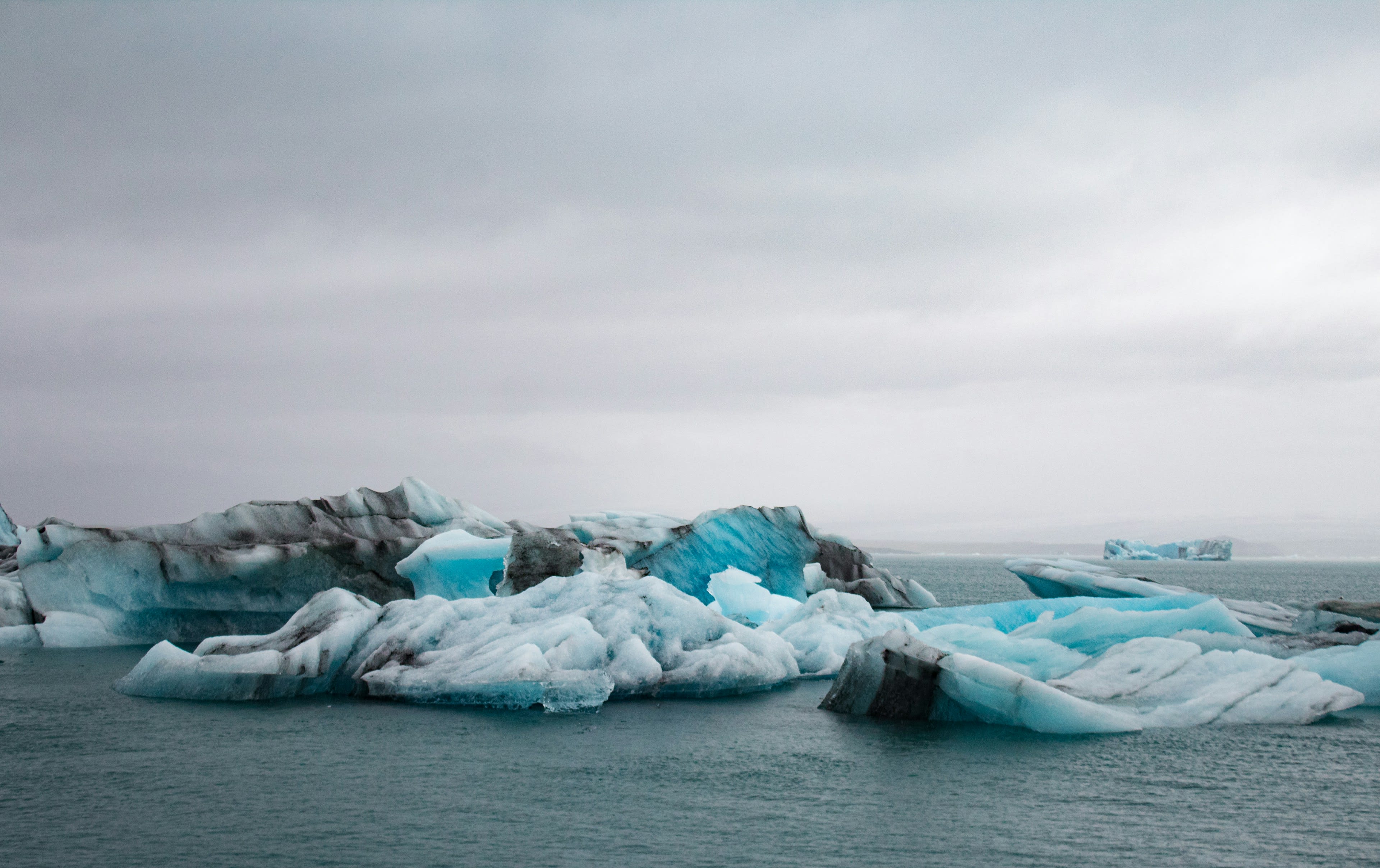 Blue and white icebergs floating in a still glacial lagoon under grey sky