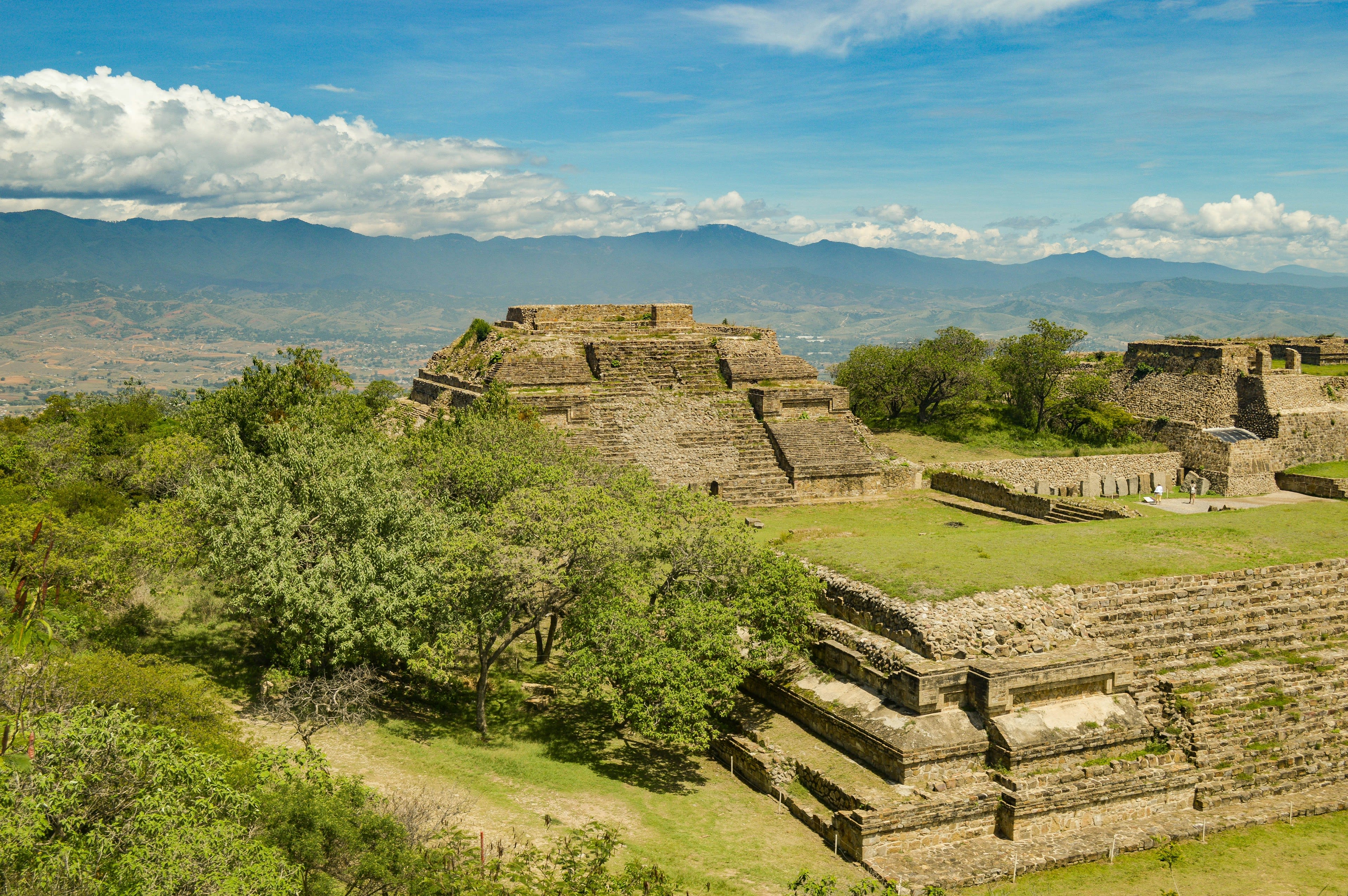 Stone pyramid platforms on a broad grassy plaza under clouds