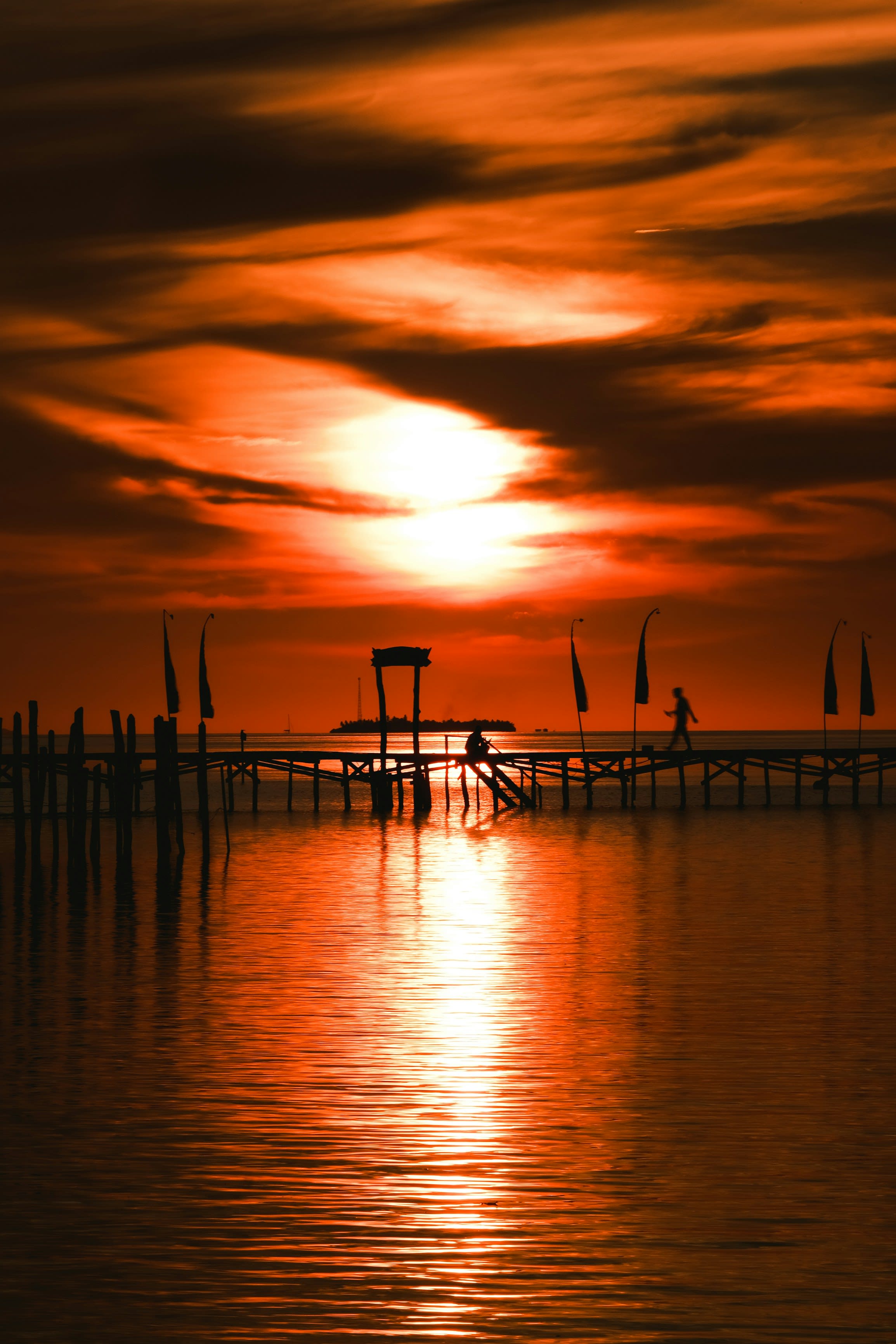 Silhouettes on a jetty under a deep red sunset over calm water