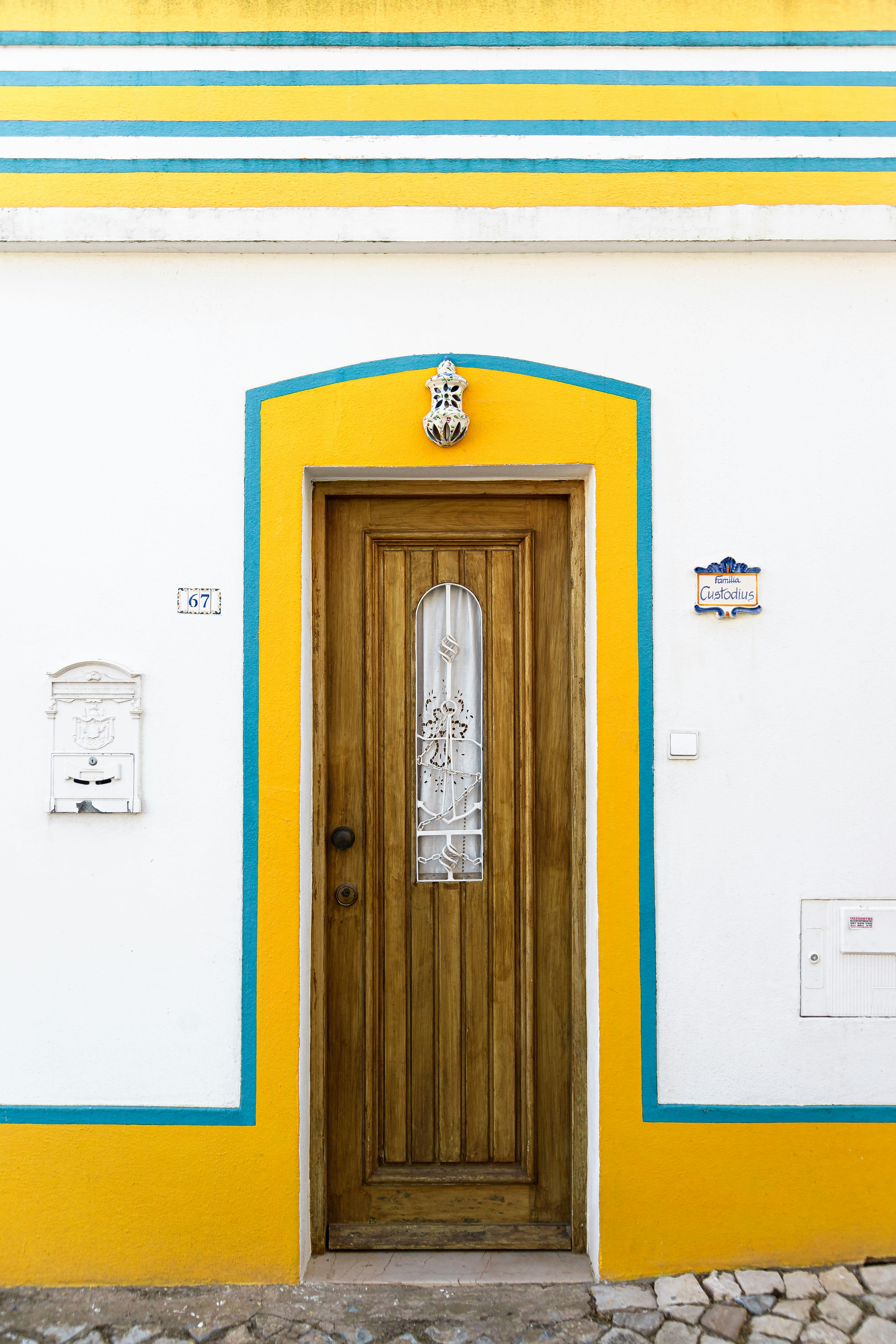 A white house with yellow trim and a wooden door in strong afternoon light