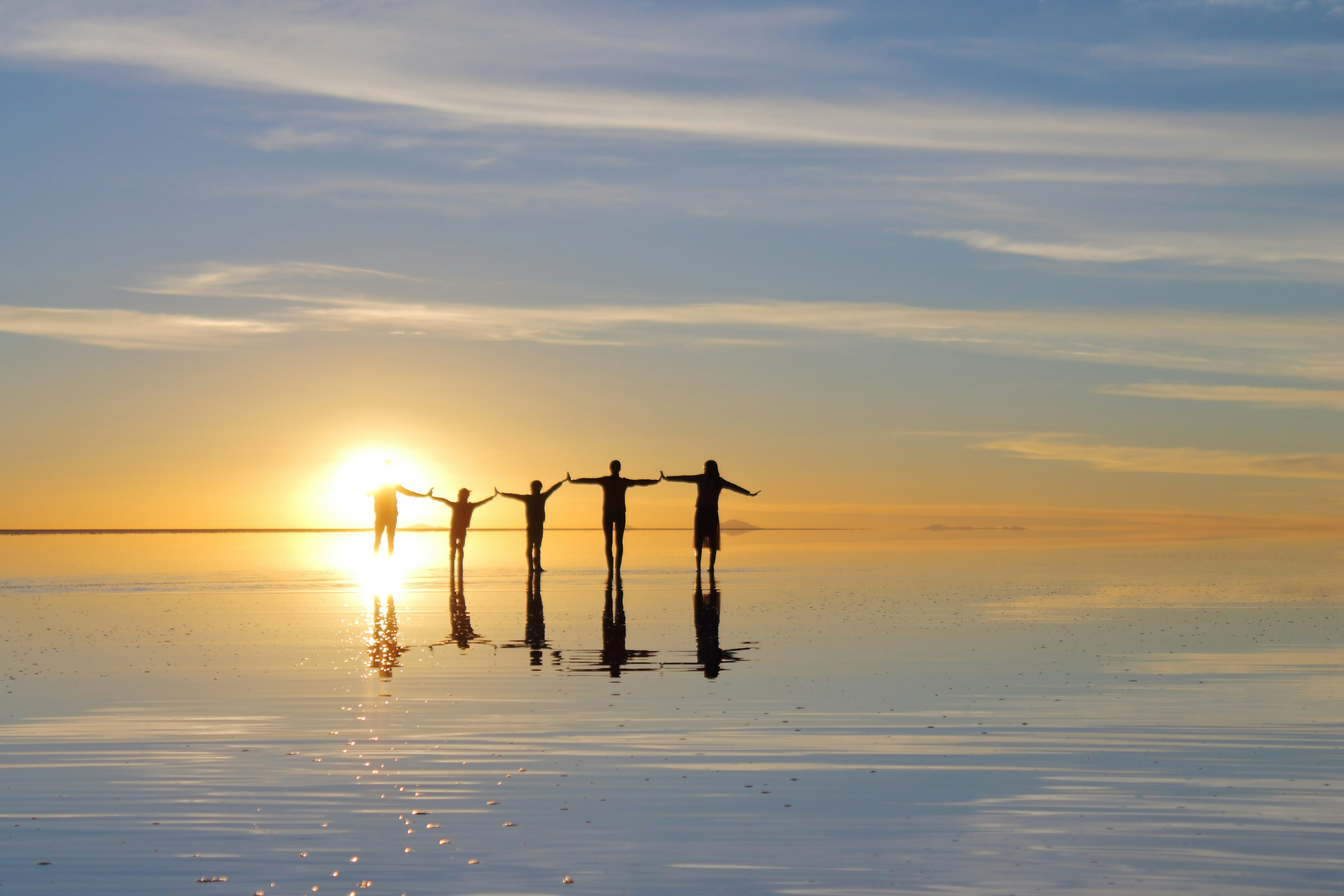 People silhouetted against a sunset reflected on the wet salt flat