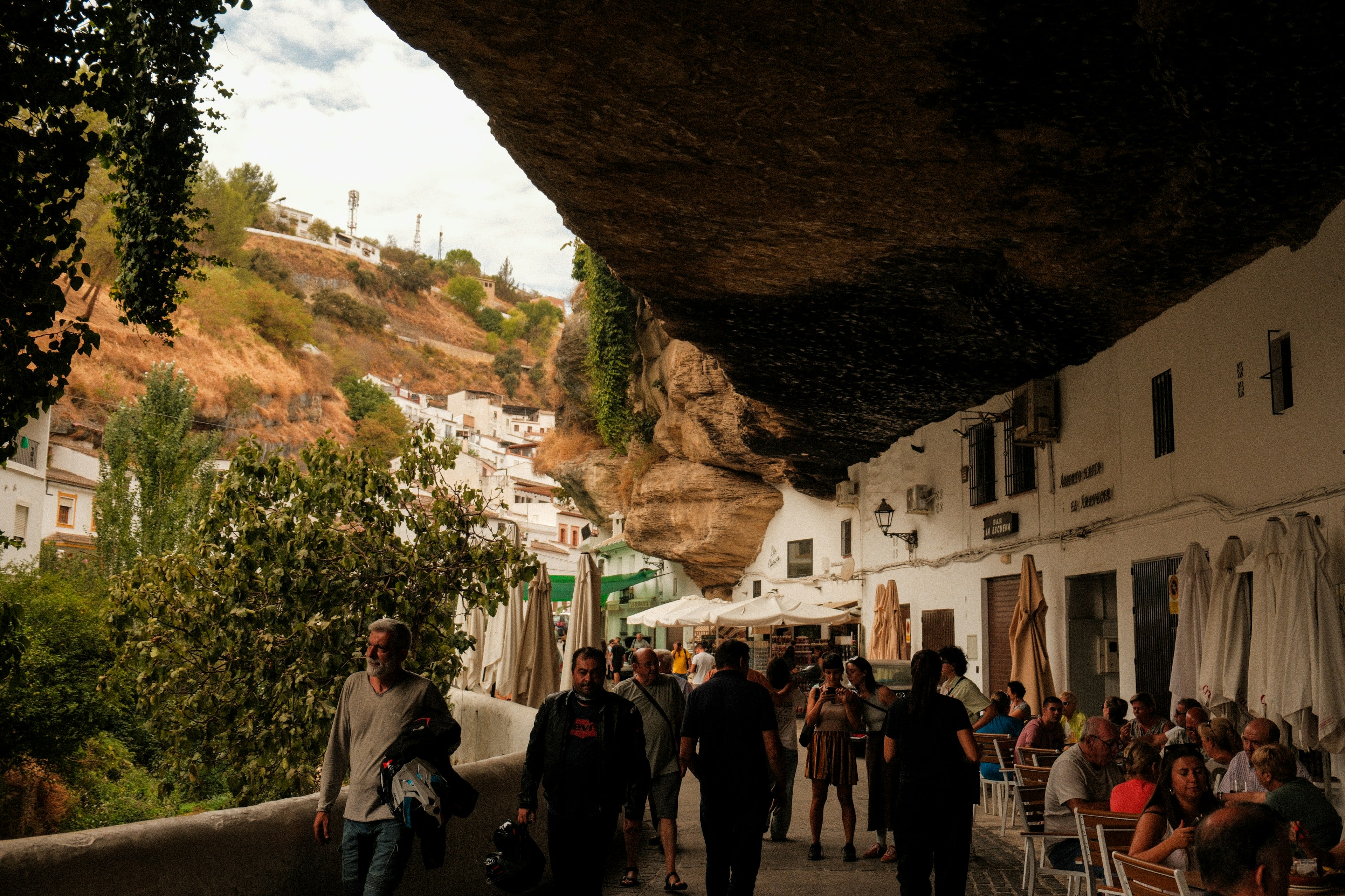 People walking a village street roofed by a massive rock overhang