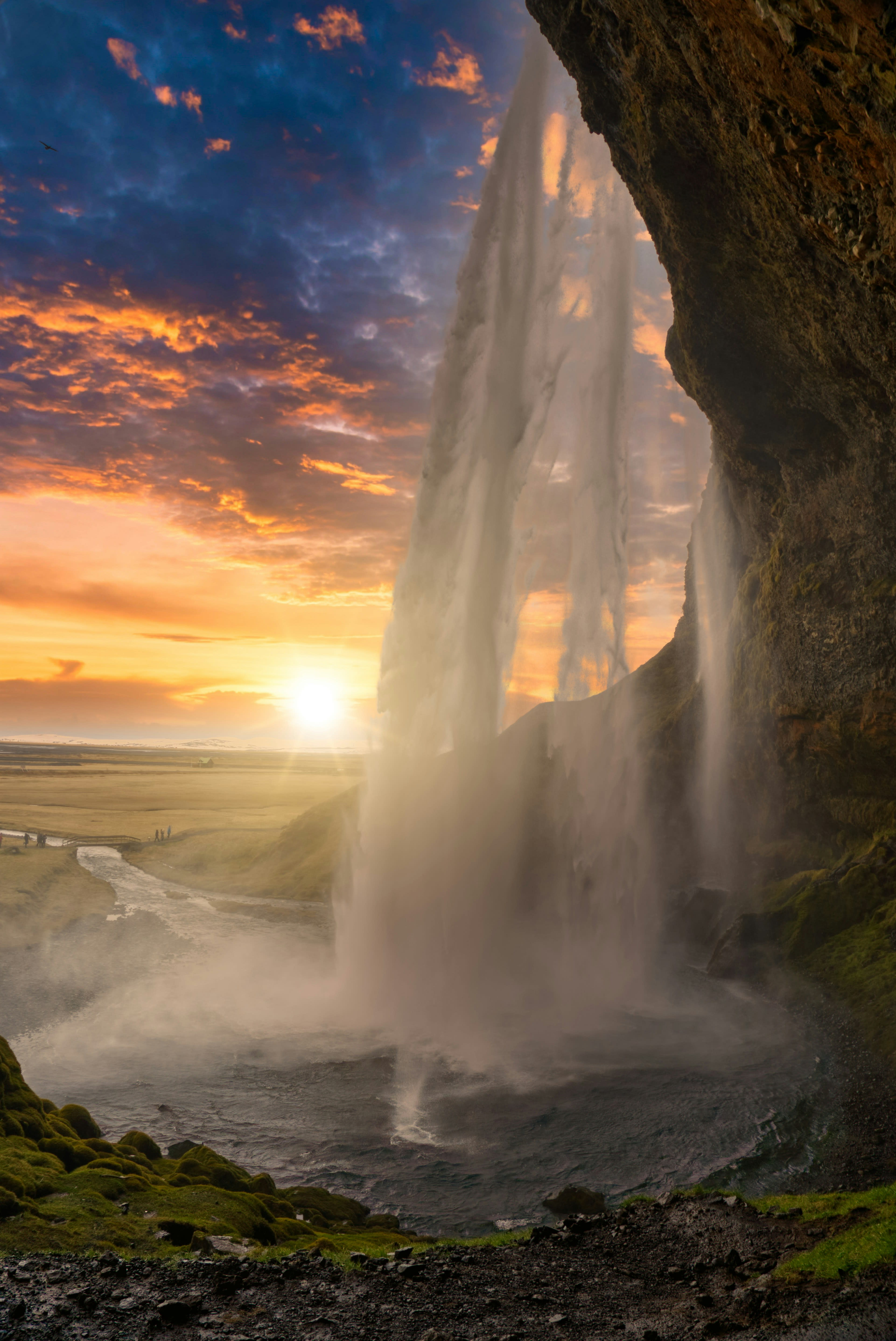 A waterfall seen from behind the curtain of water with low sun beyond it