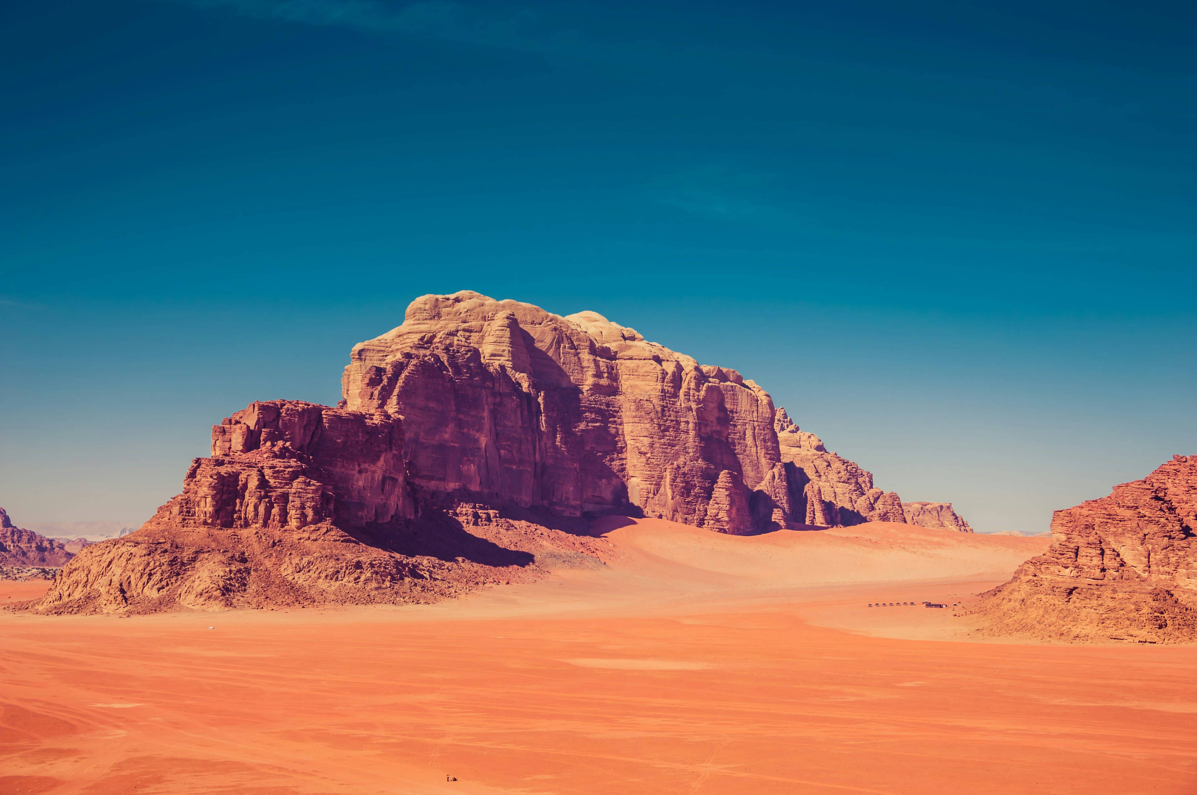 A sandstone massif lit purple and orange above red desert sand at dusk