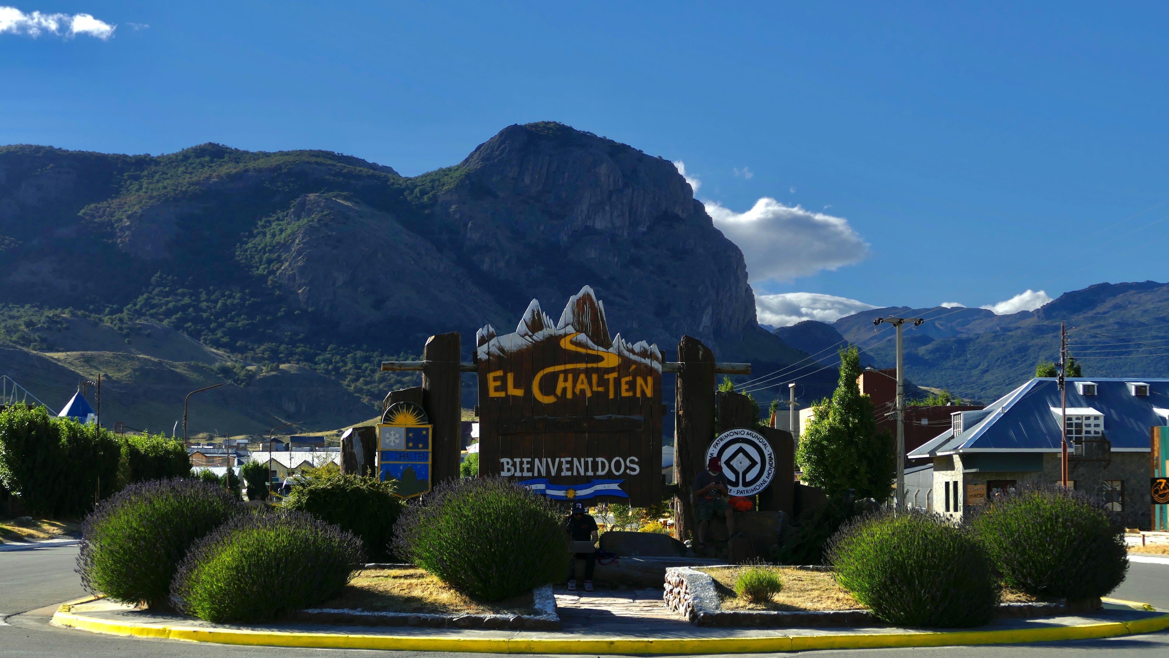 A welcome sign at the entrance to a small town with a rock massif rising behind it in evening light