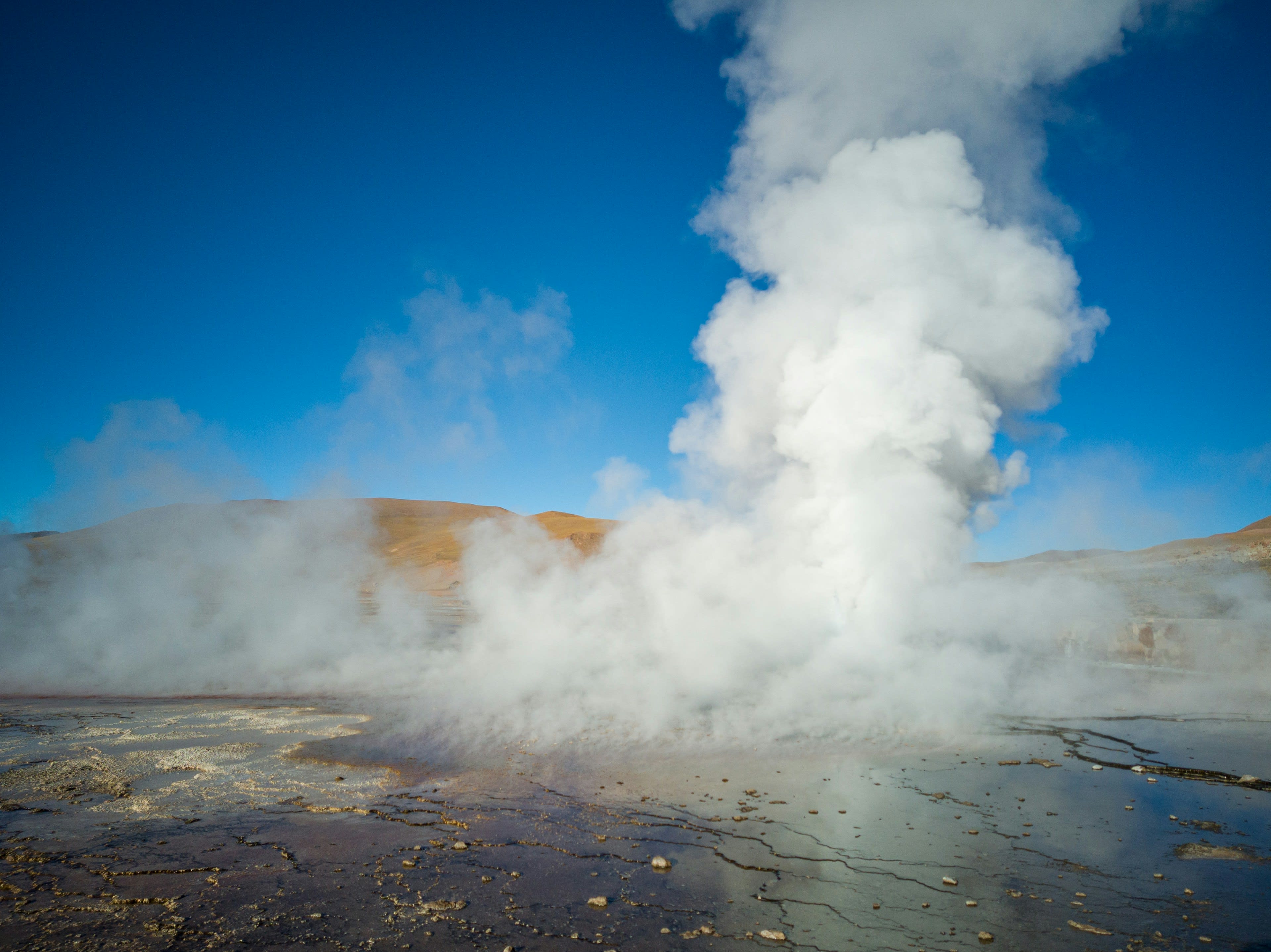 A tall column of geyser steam rising into cold blue morning air