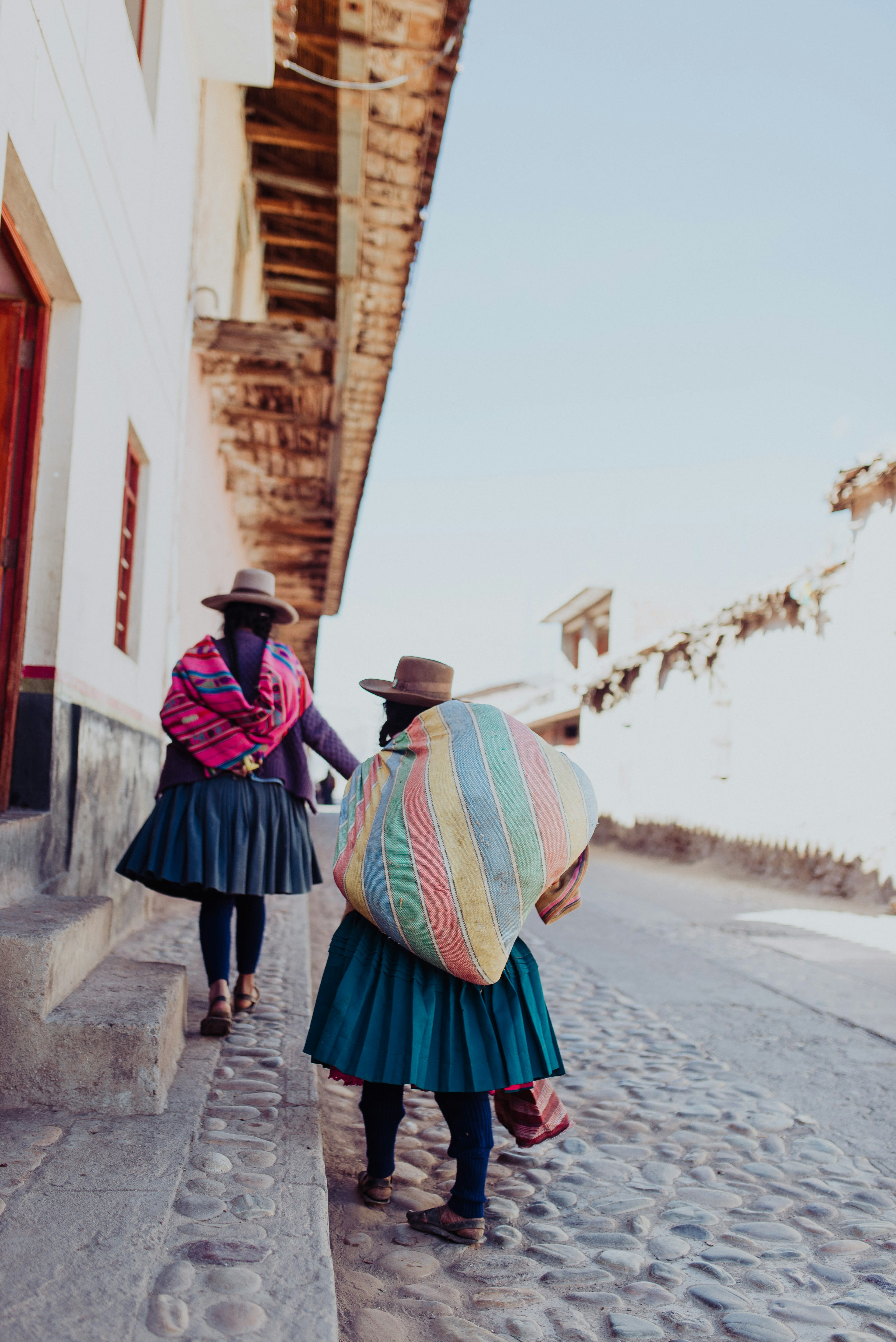 Two women carrying woven bundles walking up a cobbled Cusco street
