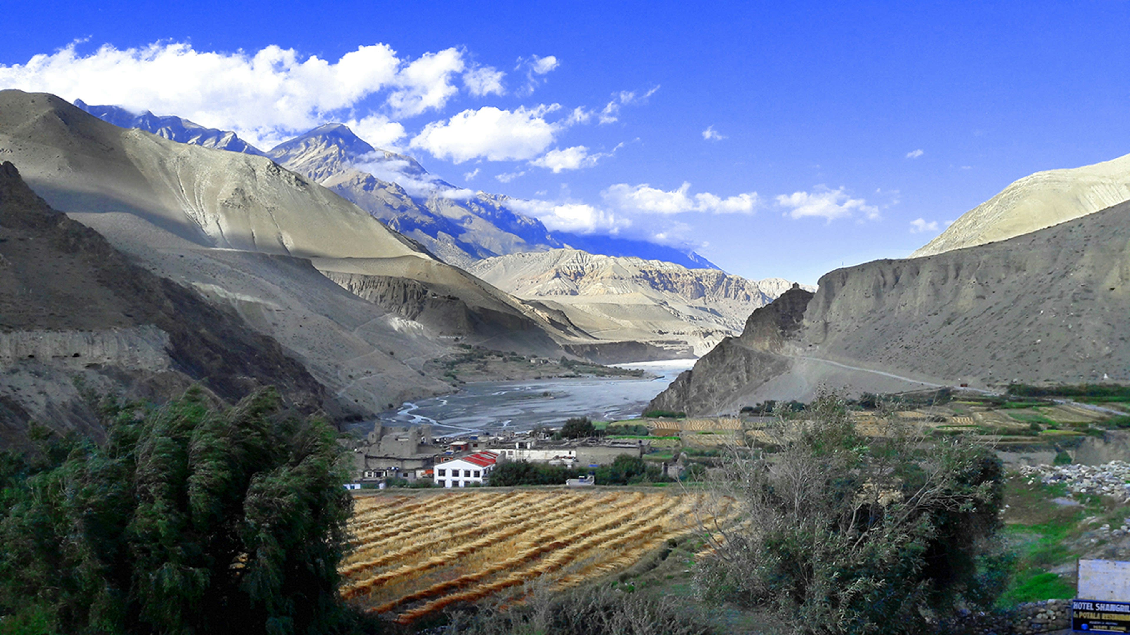 A small village of white and ochre buildings among green fields below bare eroded mountains