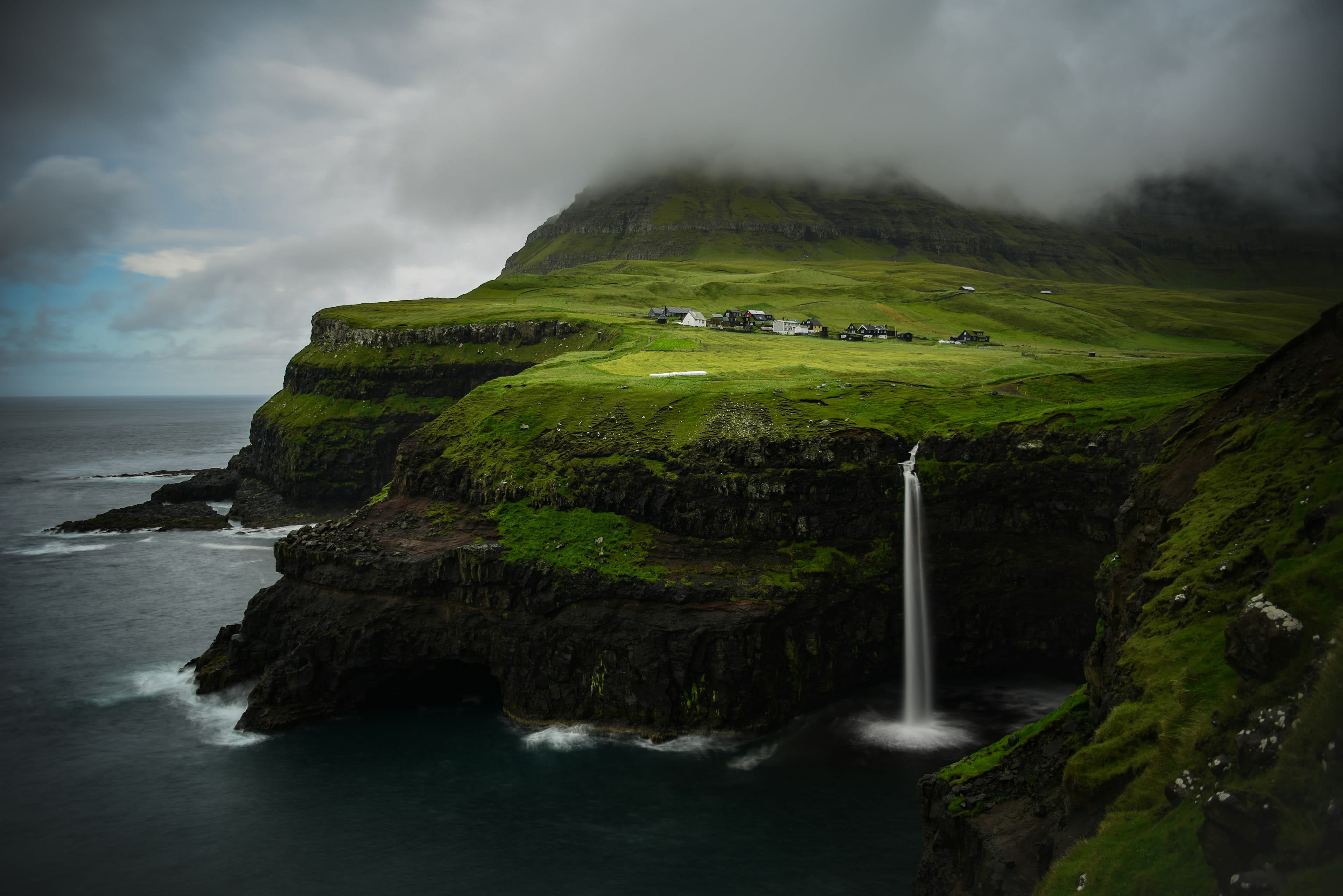A waterfall falling from a green clifftop village directly into the ocean