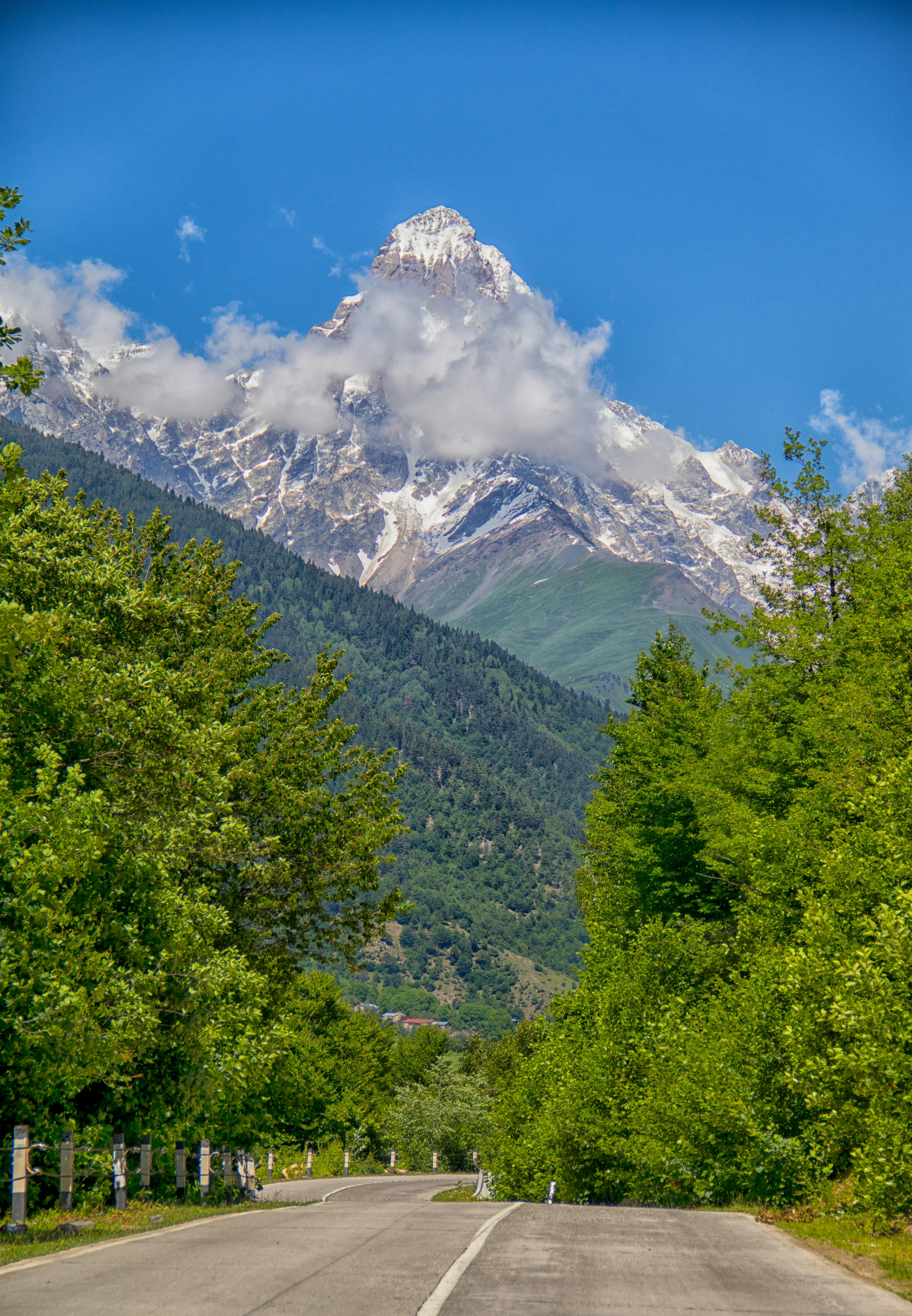 A mountain road running towards a distant snow-capped twin-peaked mountain