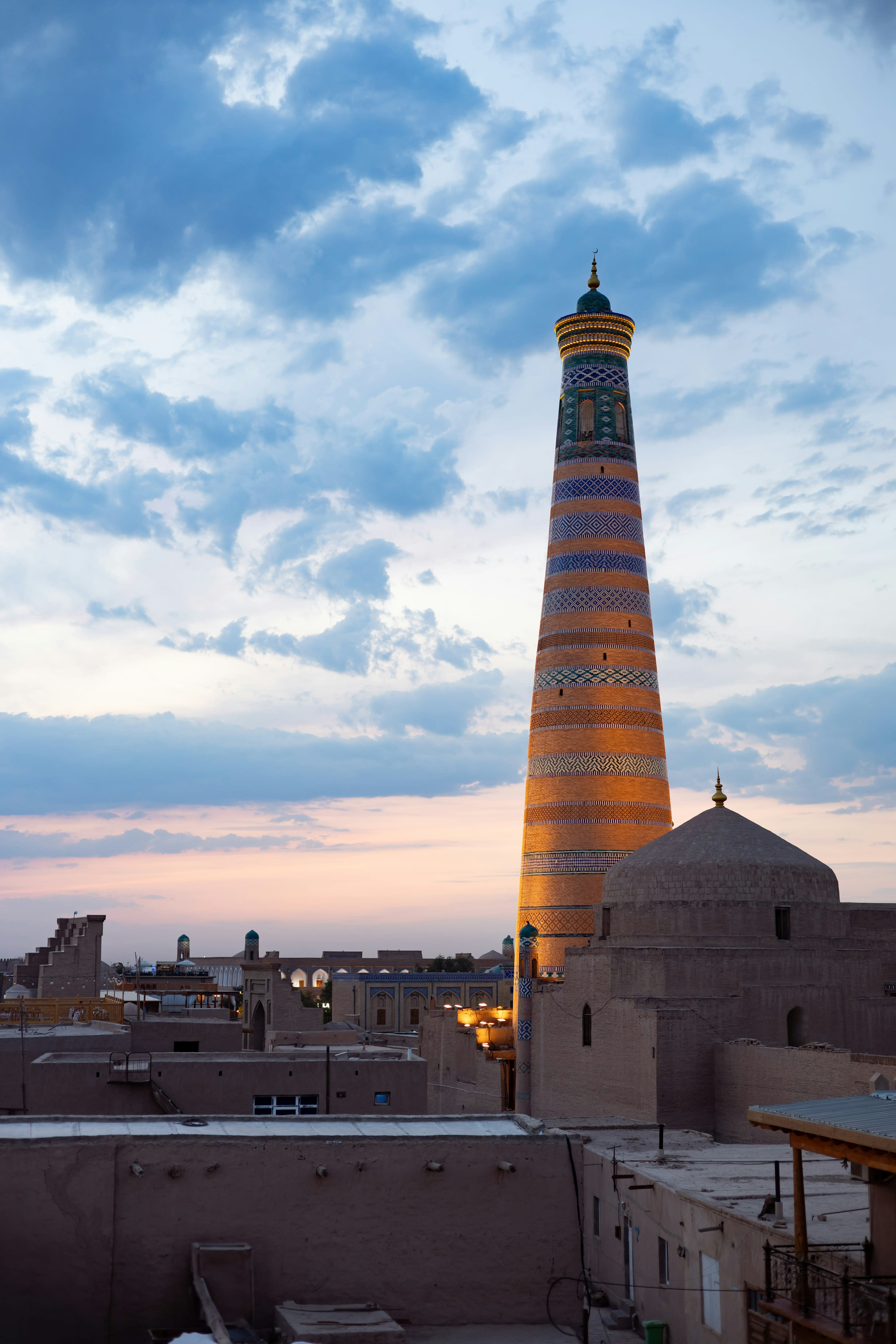 A striped minaret rising over the mud-walled old town at dusk