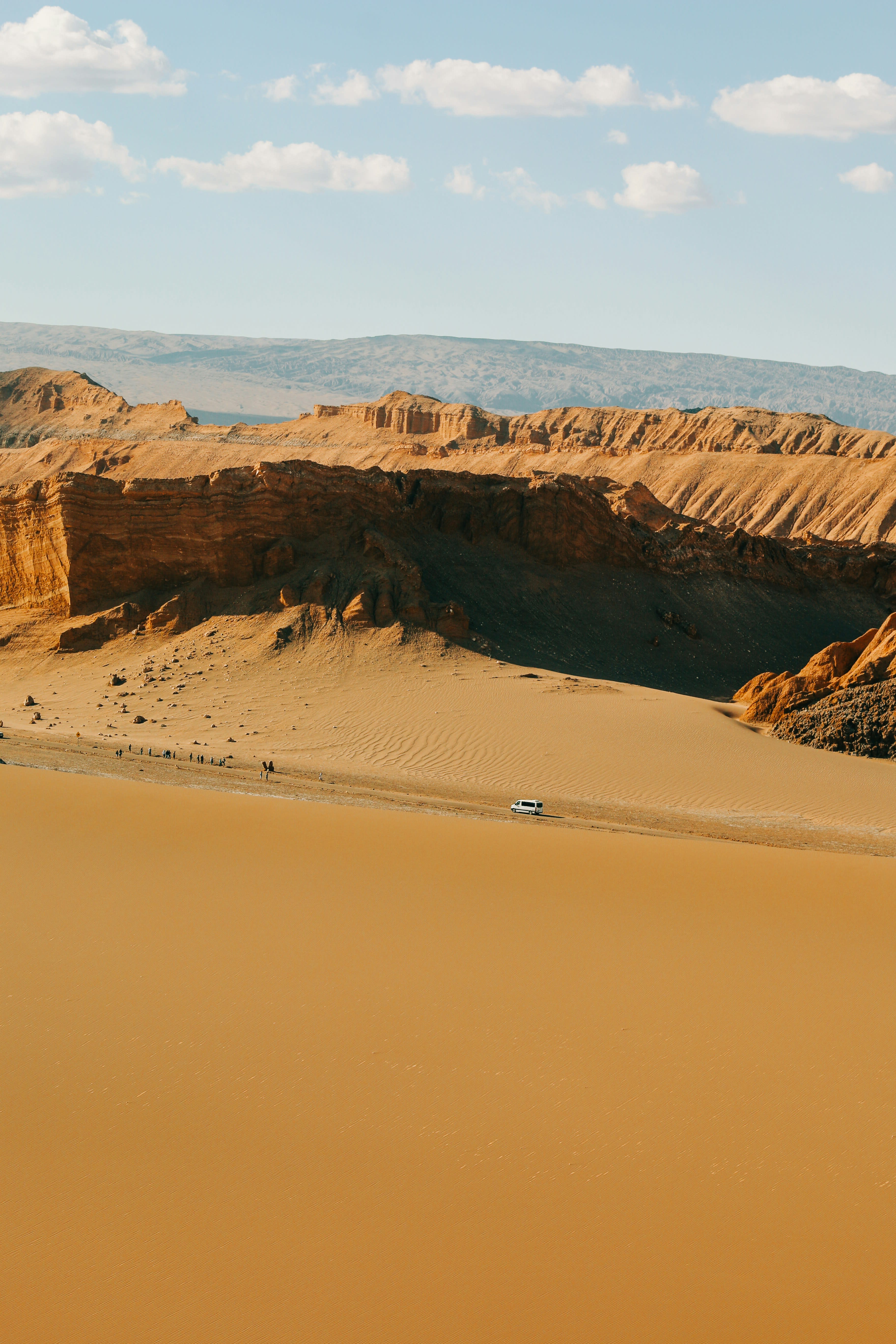 People walking single file along the ridge of a large sand dune