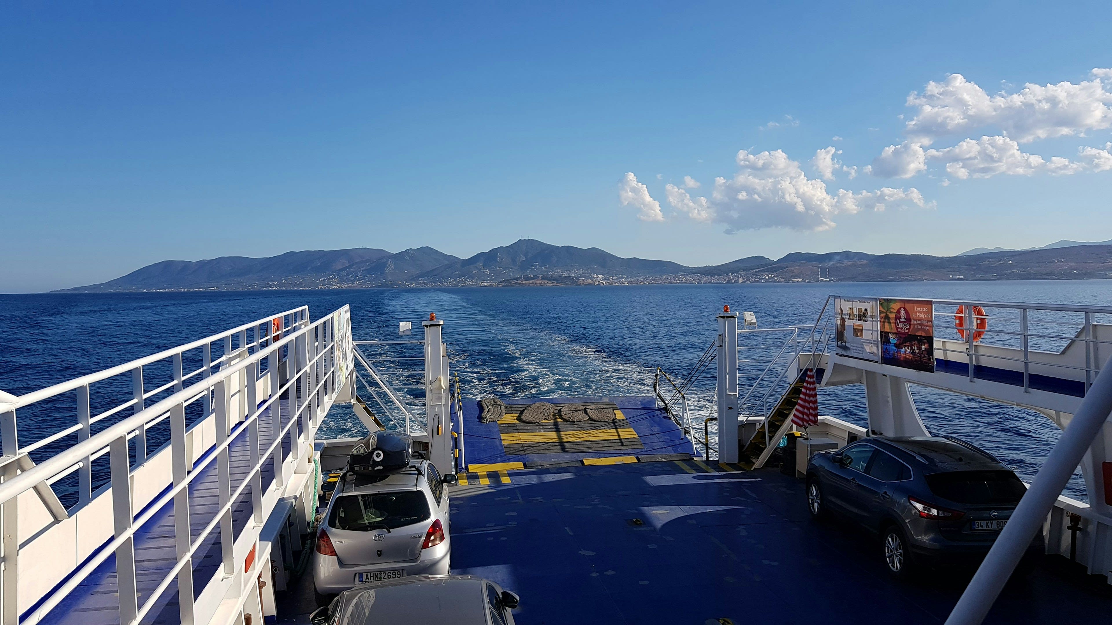 View from a ferry deck across cars and calm blue sea