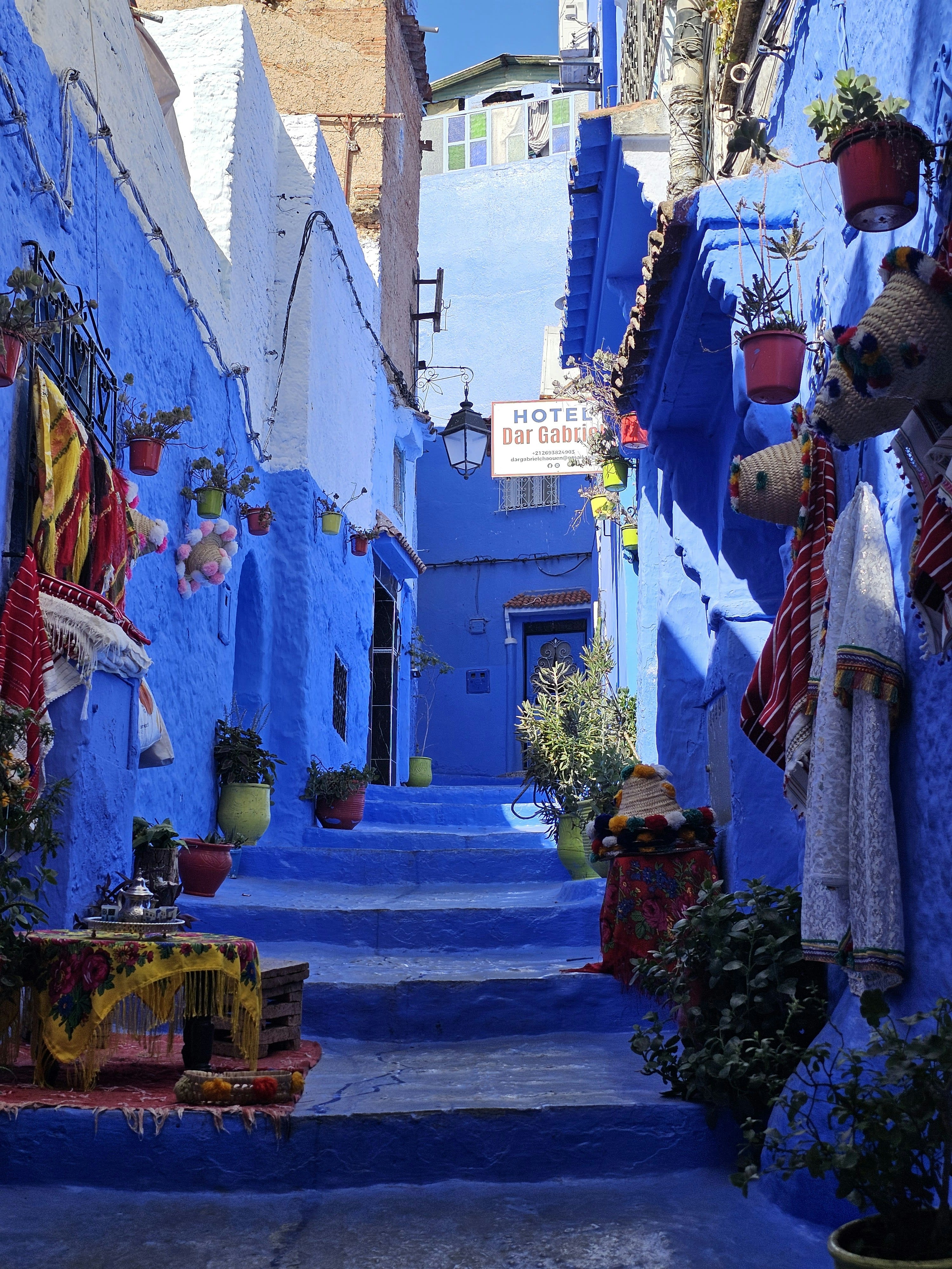 A narrow blue-painted stairway between houses with hanging textiles
