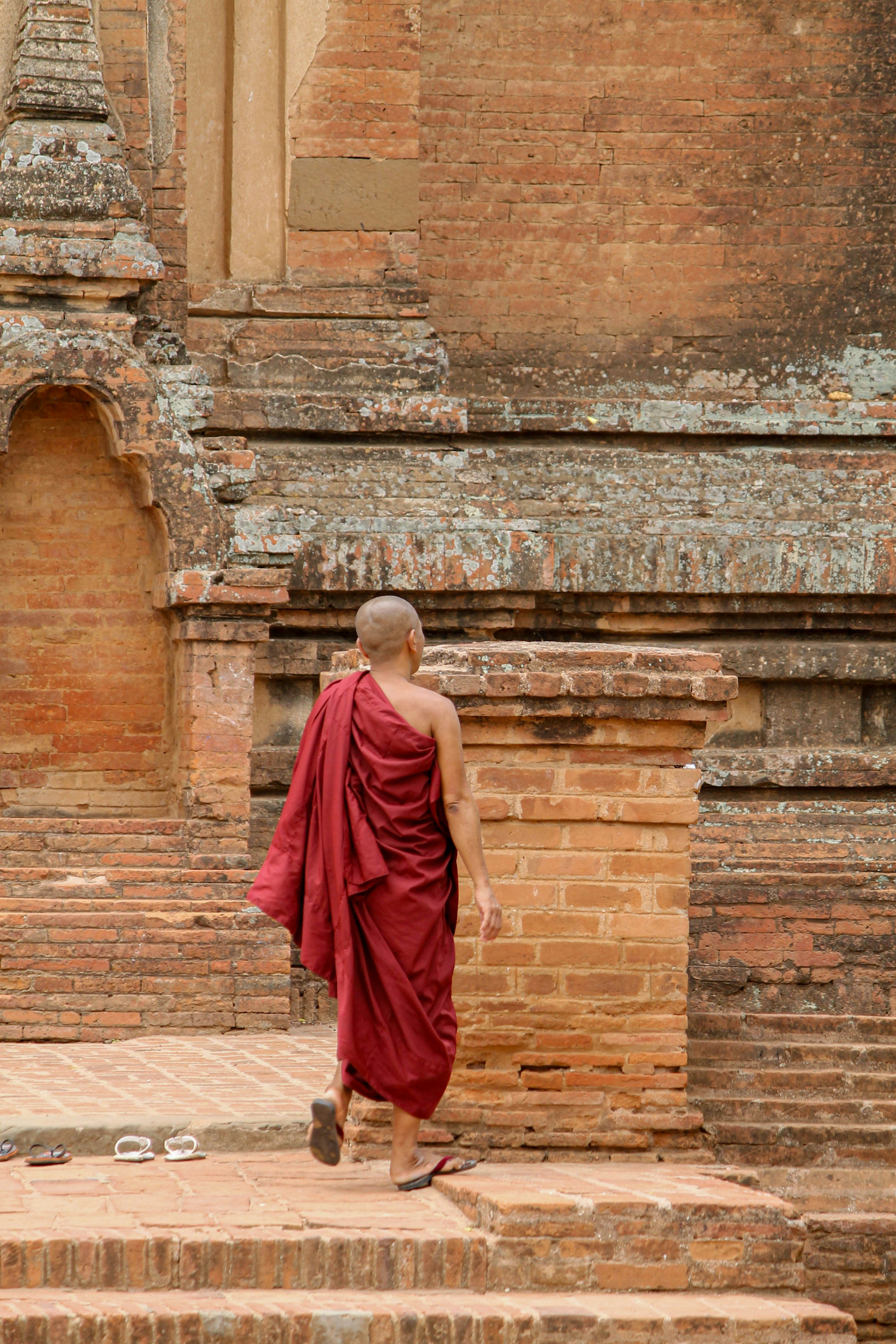 A monk in dark red robes climbing the brick steps of a Bagan temple