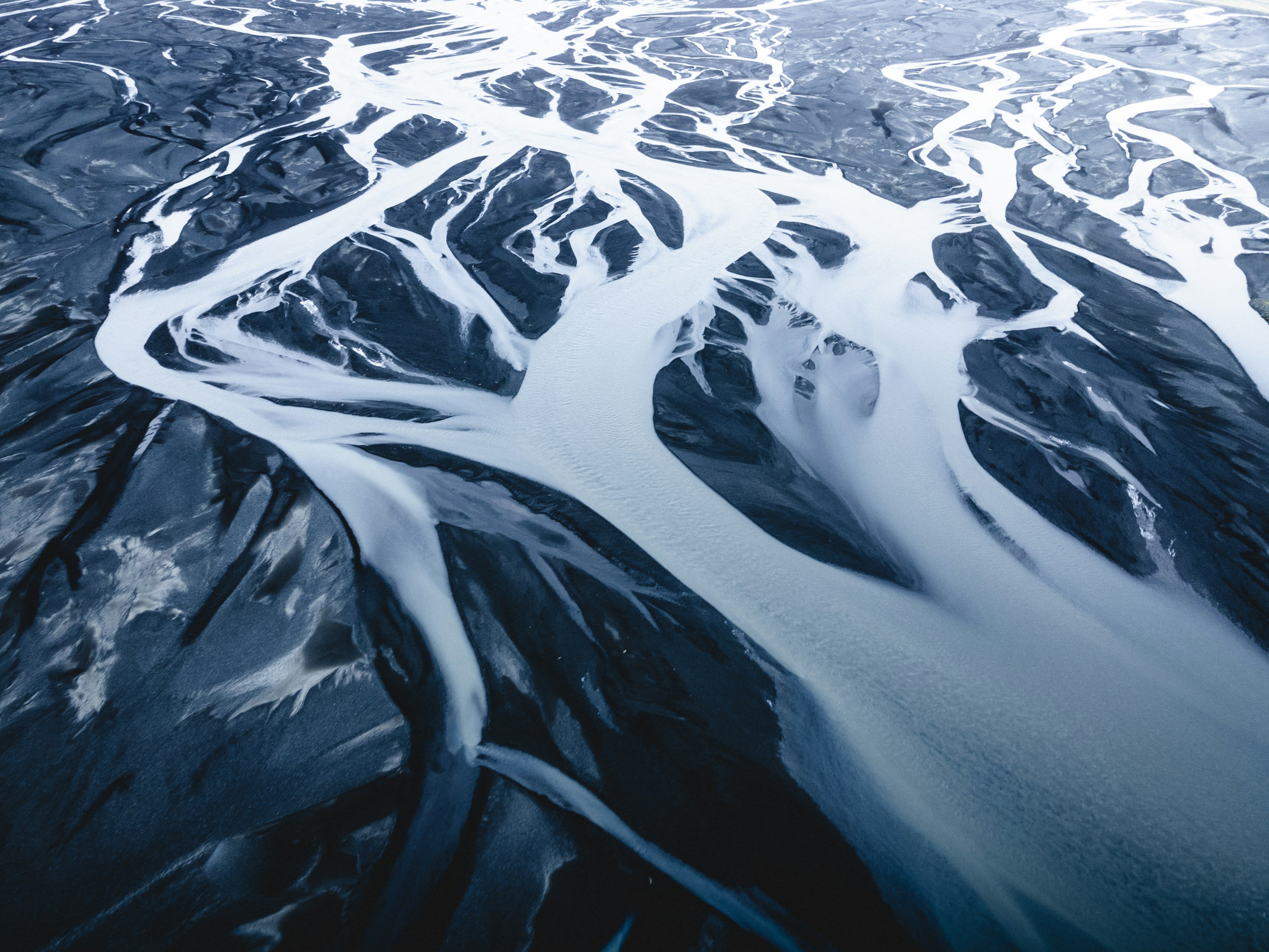 Aerial view of a silver braided river running through dark volcanic sand
