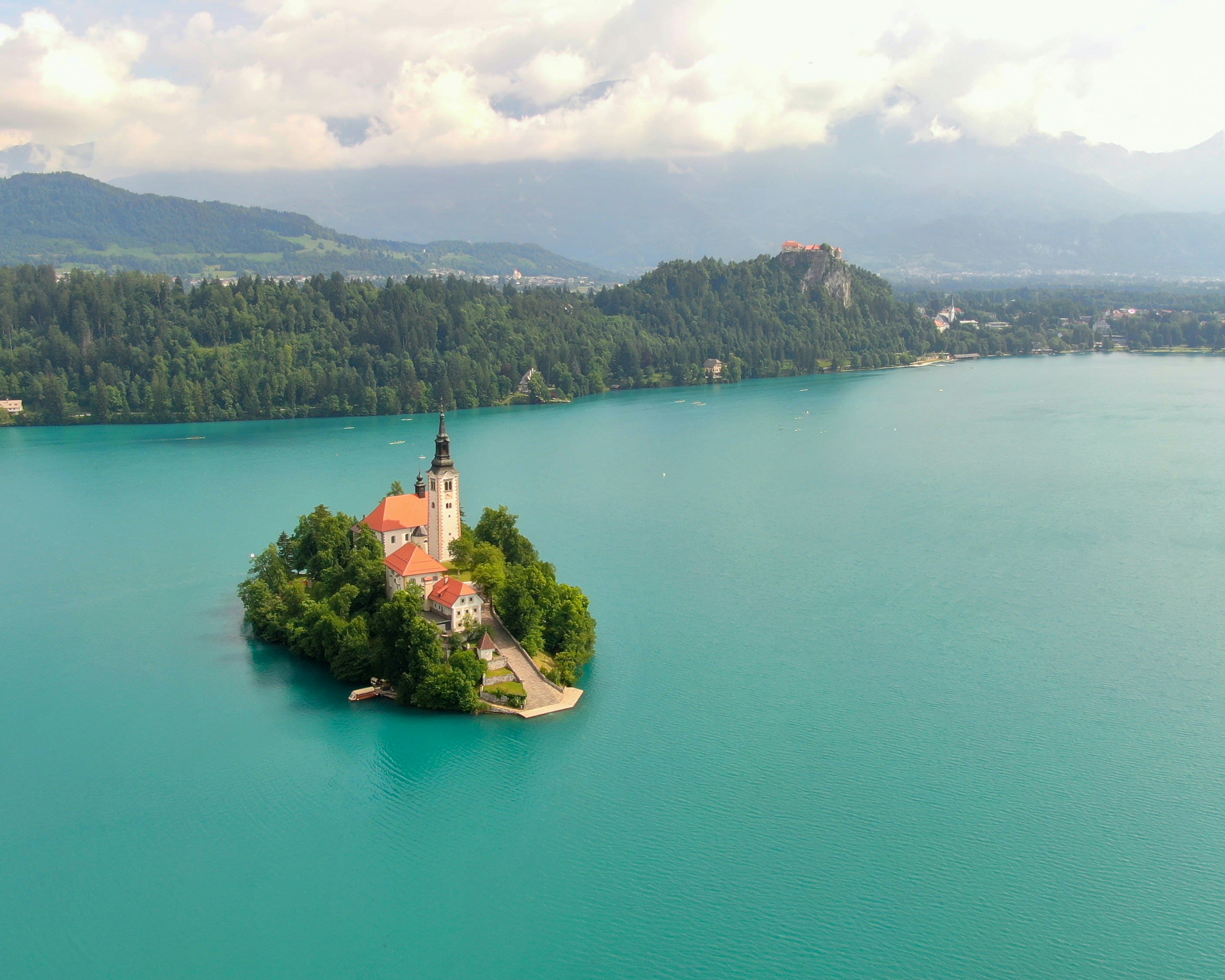 A small island with a church in the middle of a green alpine lake