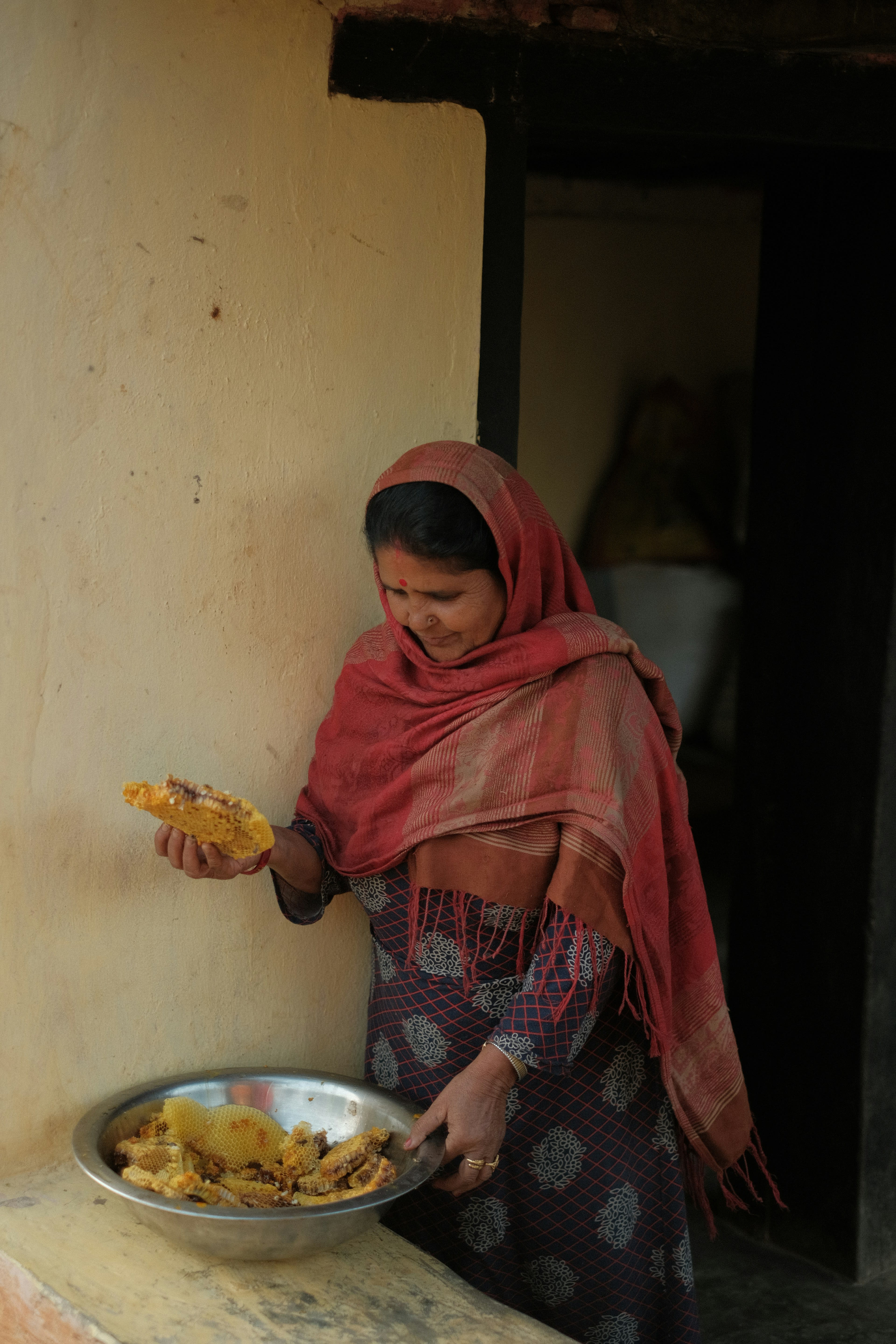 A woman preparing food in a dim traditional kitchen lit from one small window