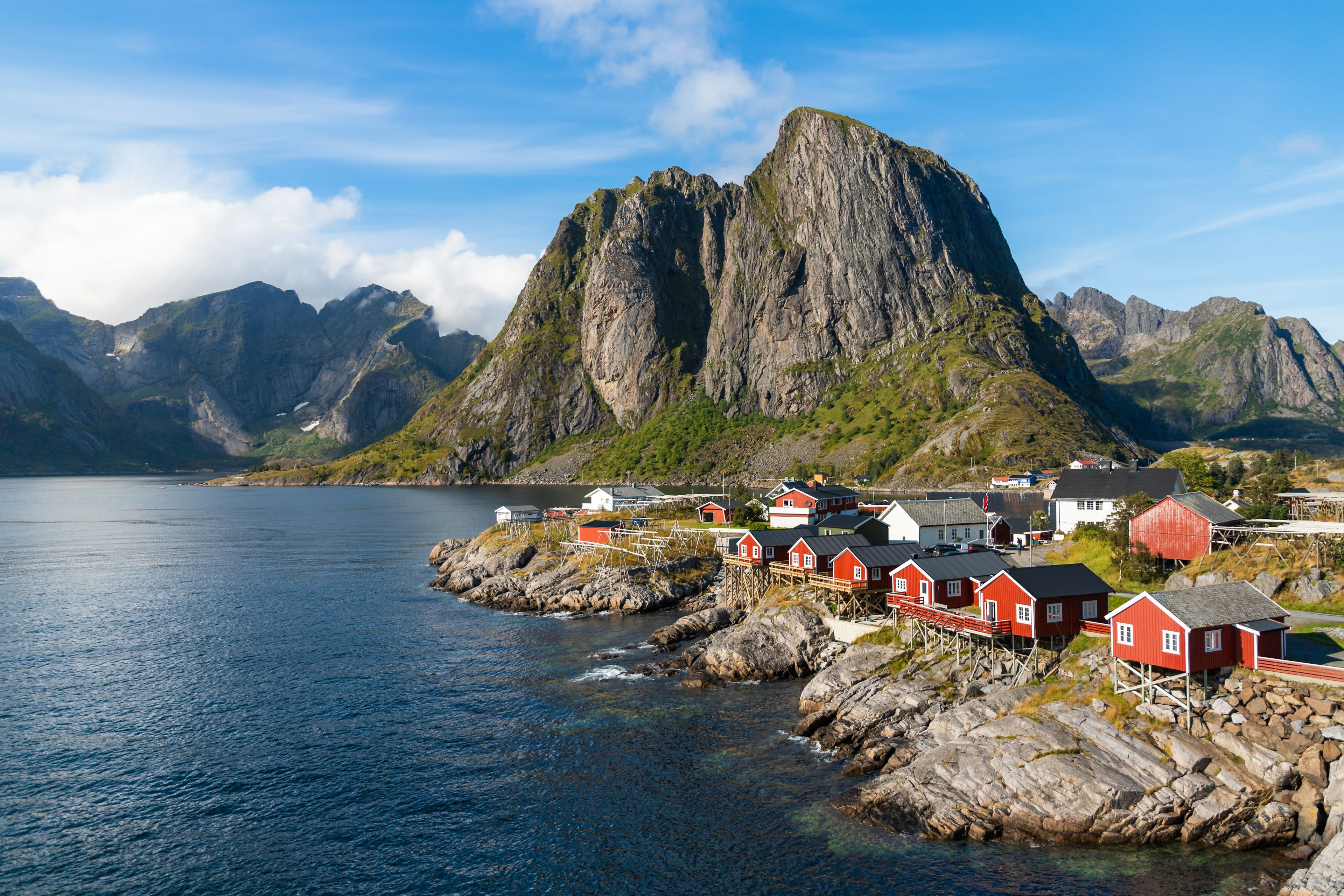 Red wooden fishermen's cabins on stilts below a steep granite mountain