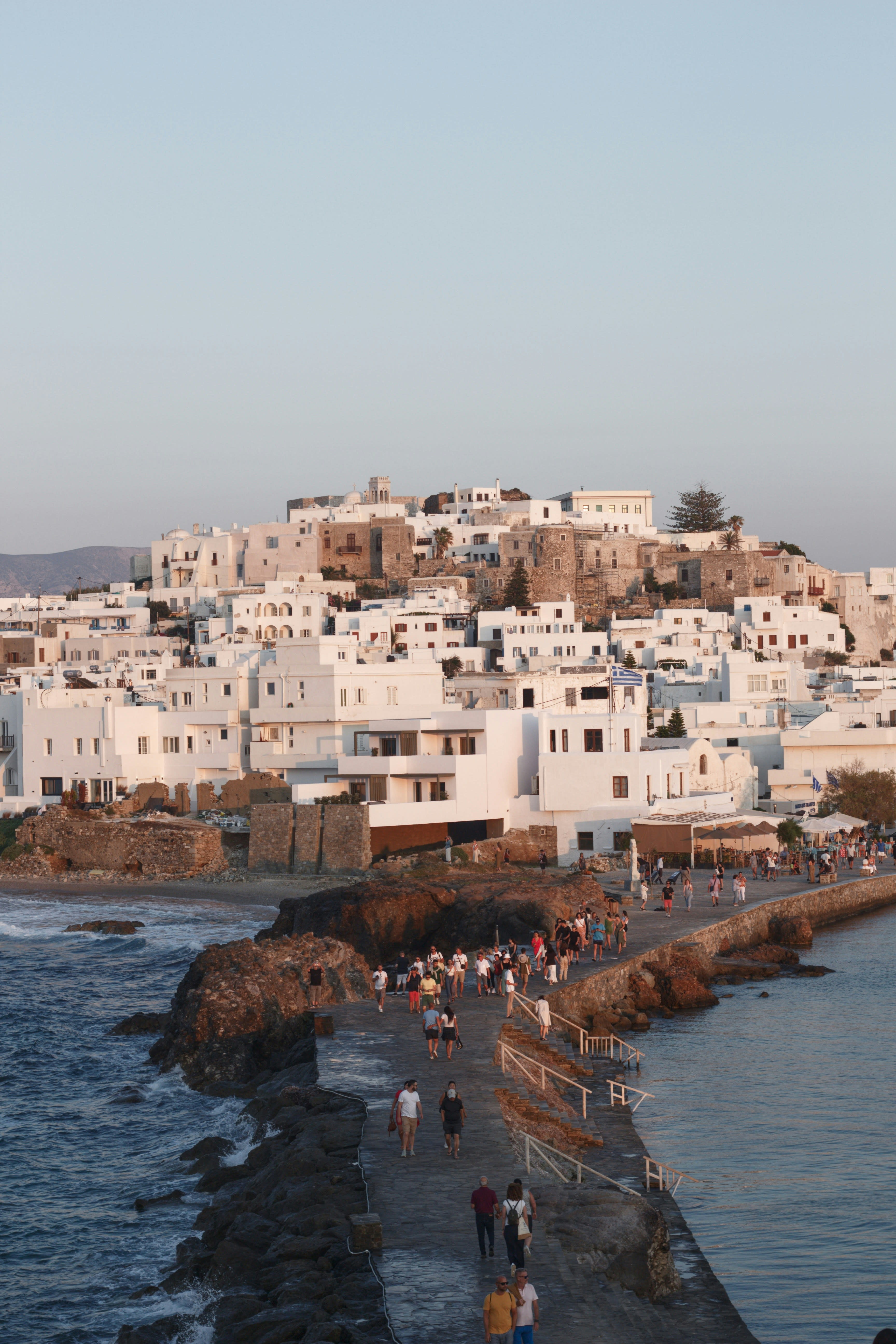 People walking a stone causeway by the sea in low evening light