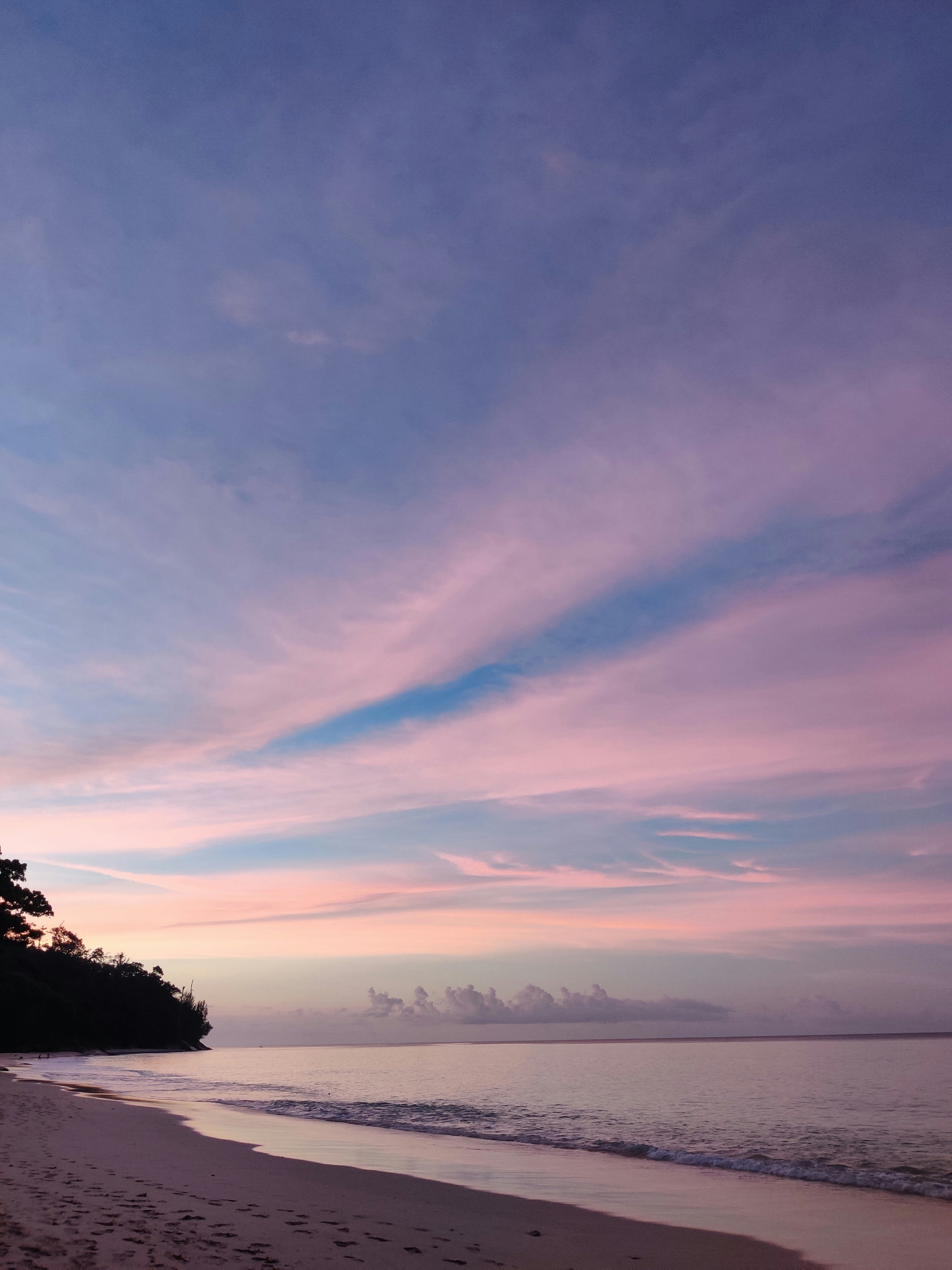 A quiet beach at dawn under a pink sky, with footprints in the sand