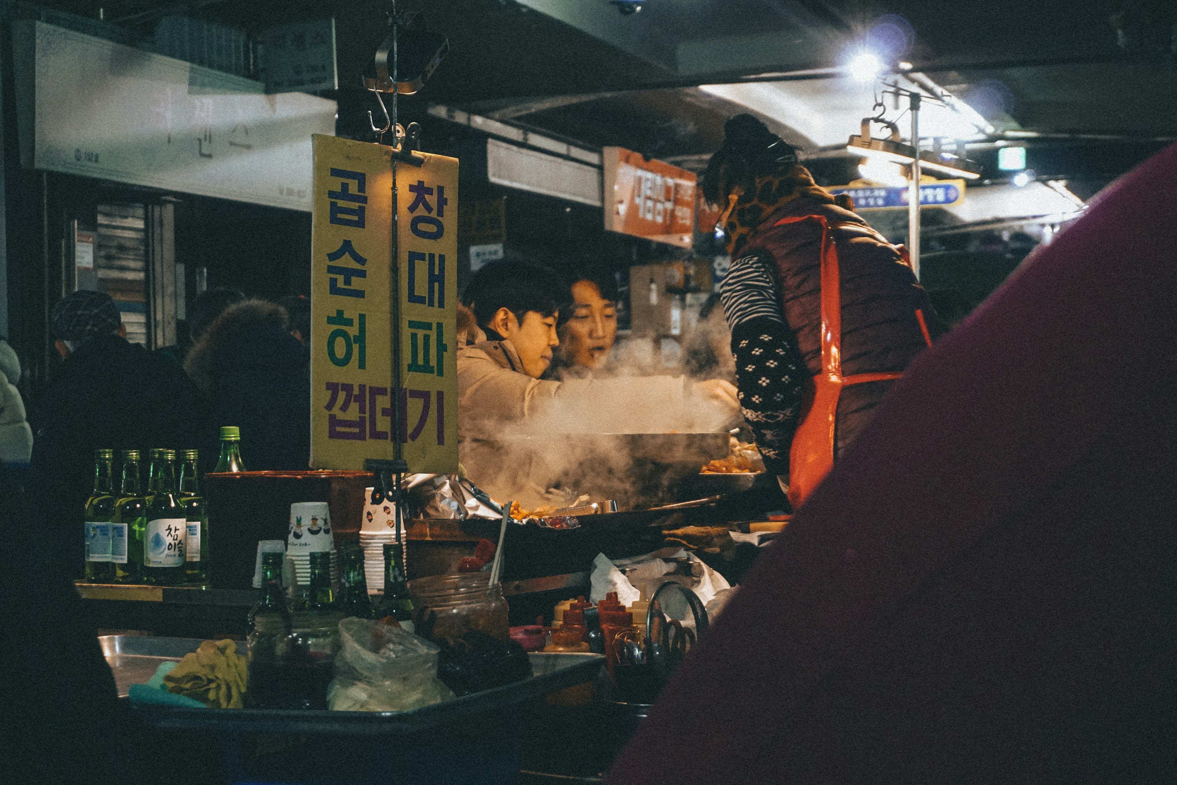 A busy market food stall with cooks working over pans under warm light