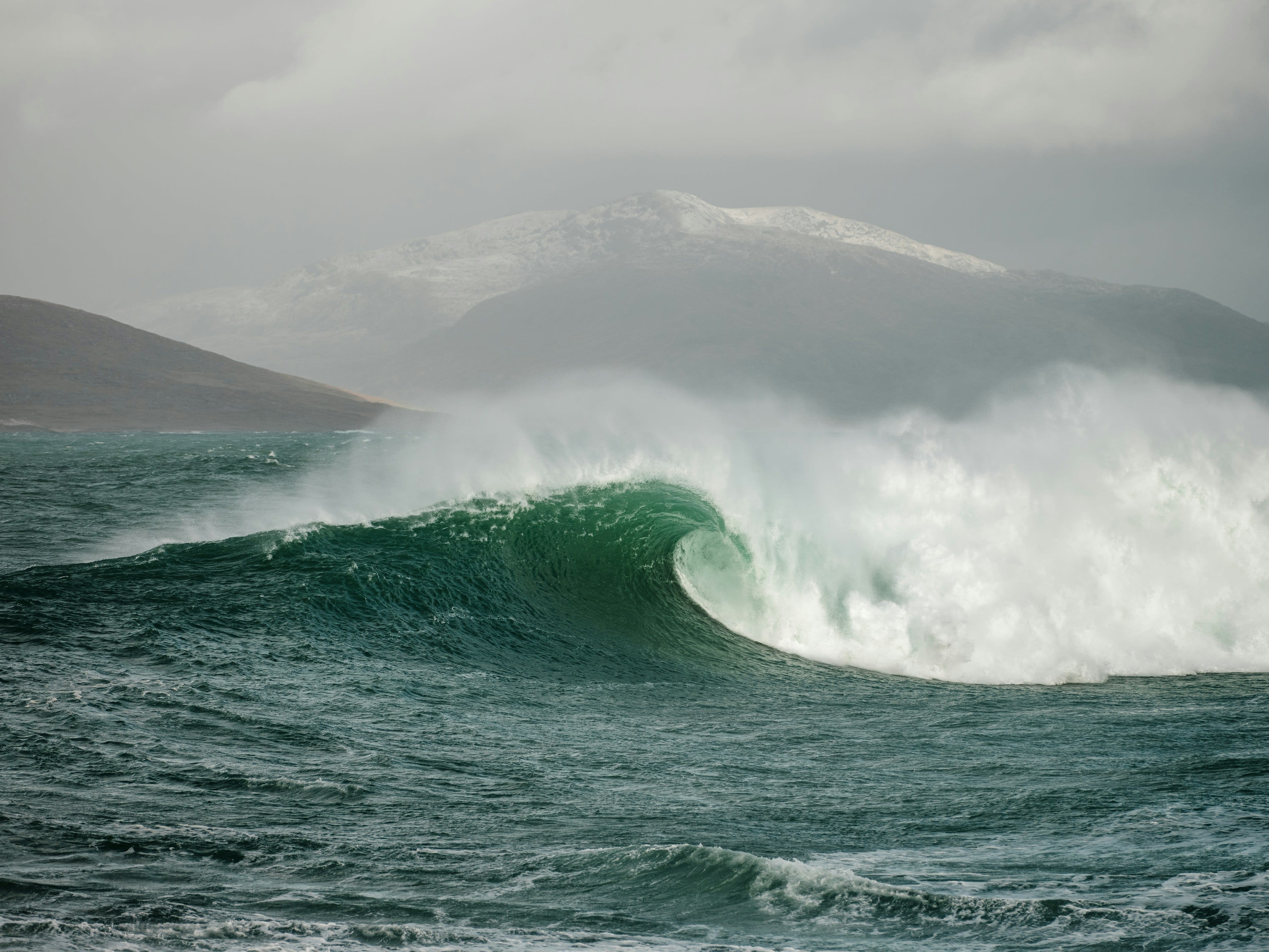 A large green wave breaking against the coast in a storm