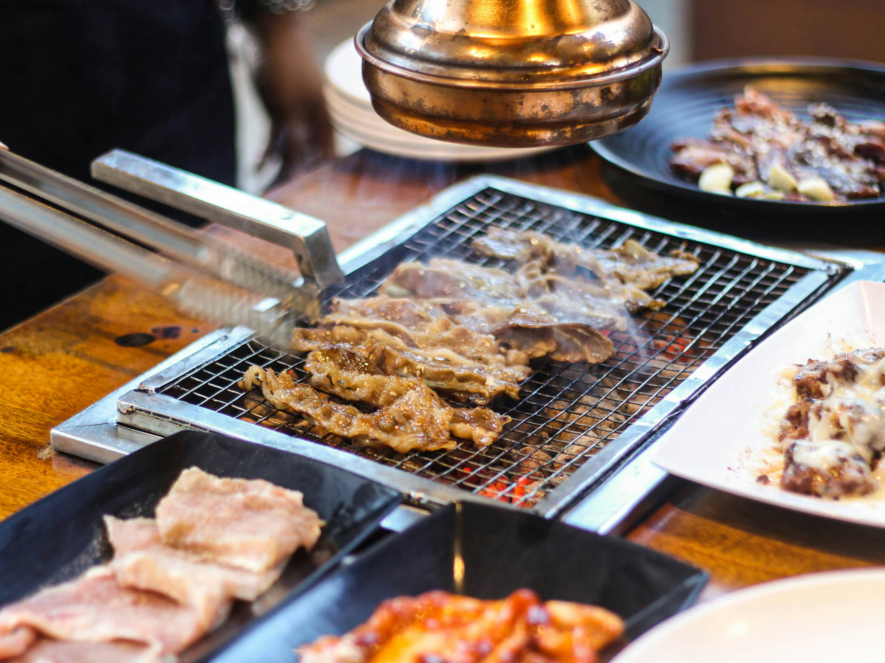 Strips of pork and kimchi cooking on a tabletop grill with side dishes around it