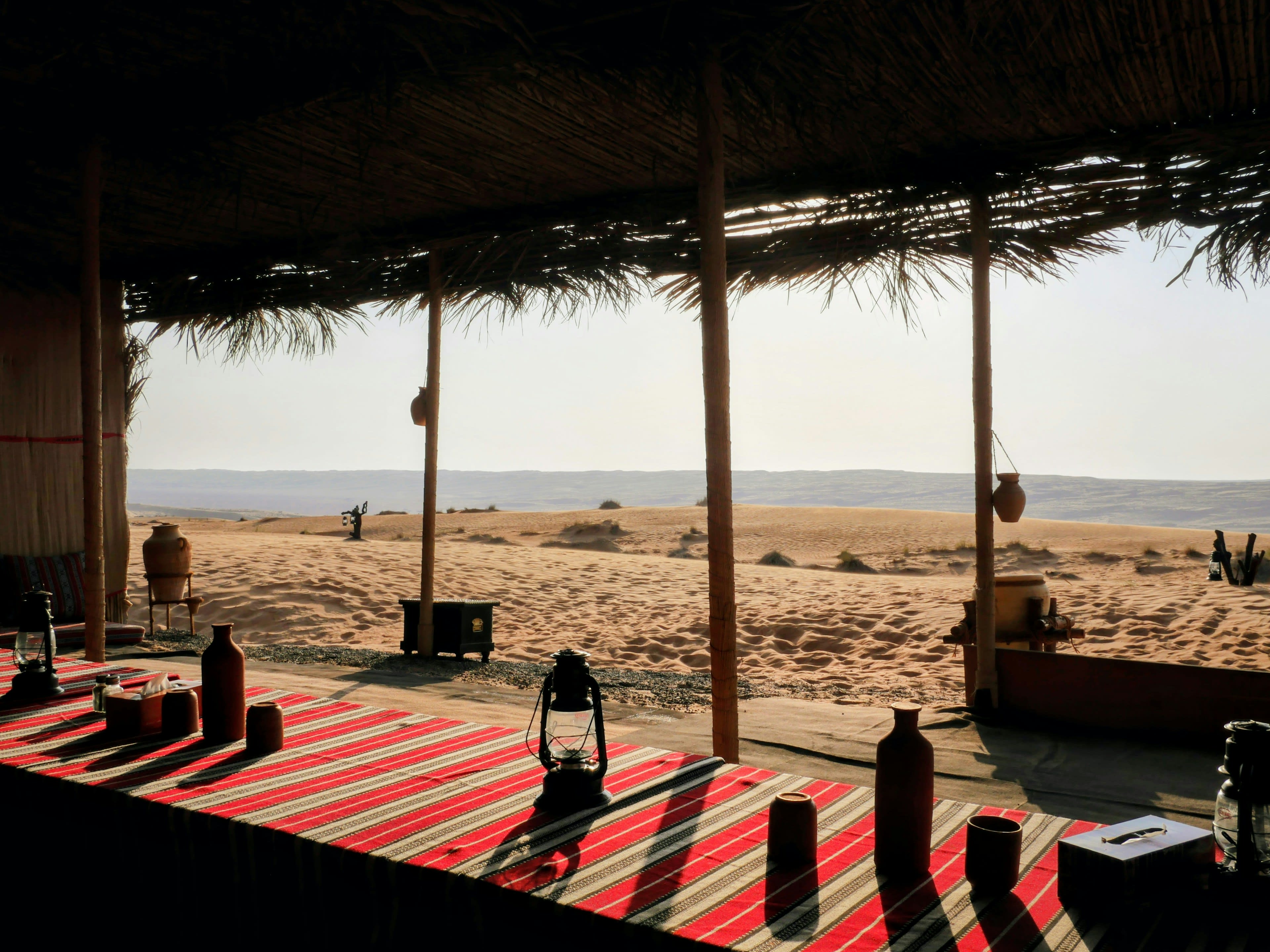 A shaded seating area with striped rugs and cushions looking out over desert sand