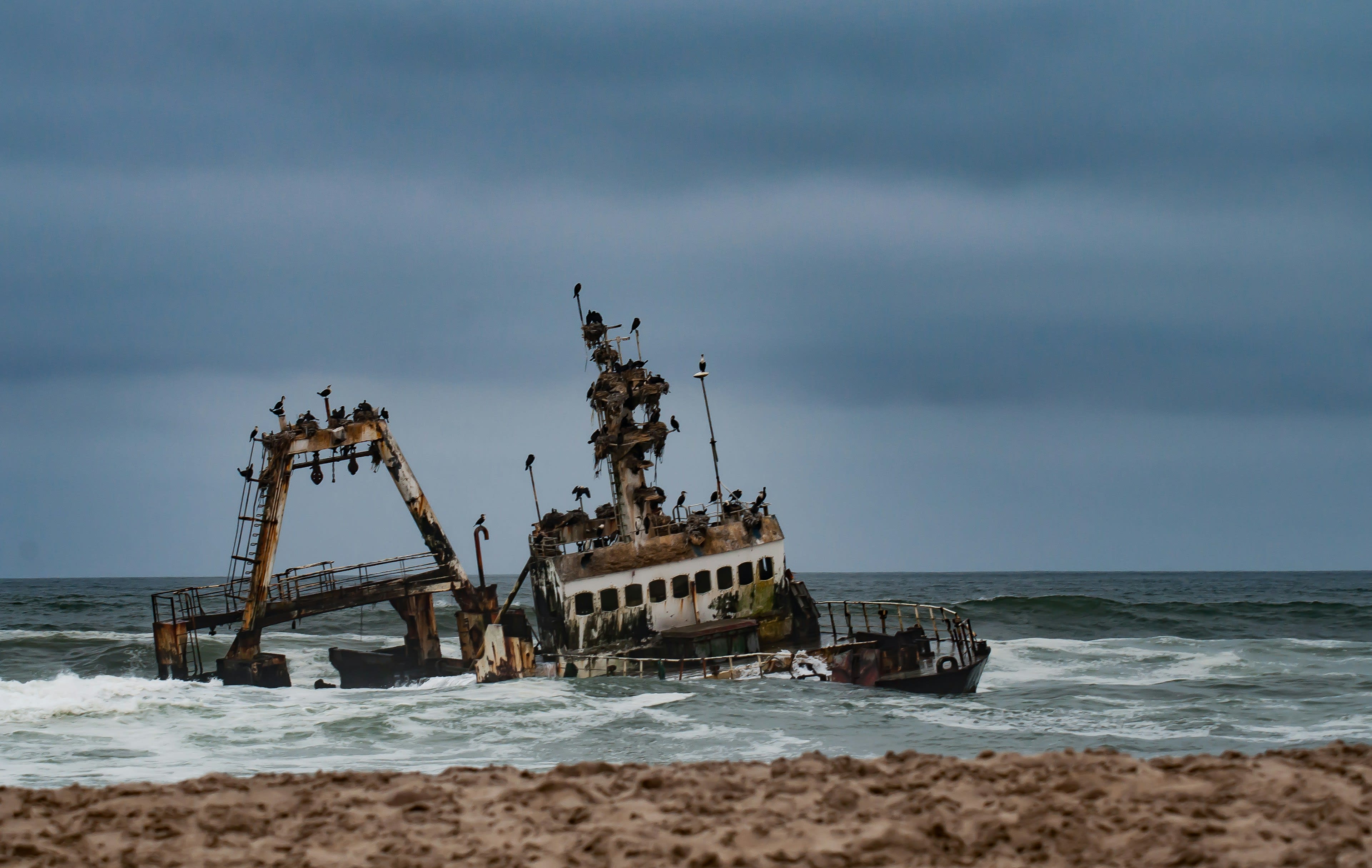 The rusting hull of a wrecked ship standing in shallow surf off a sand shore