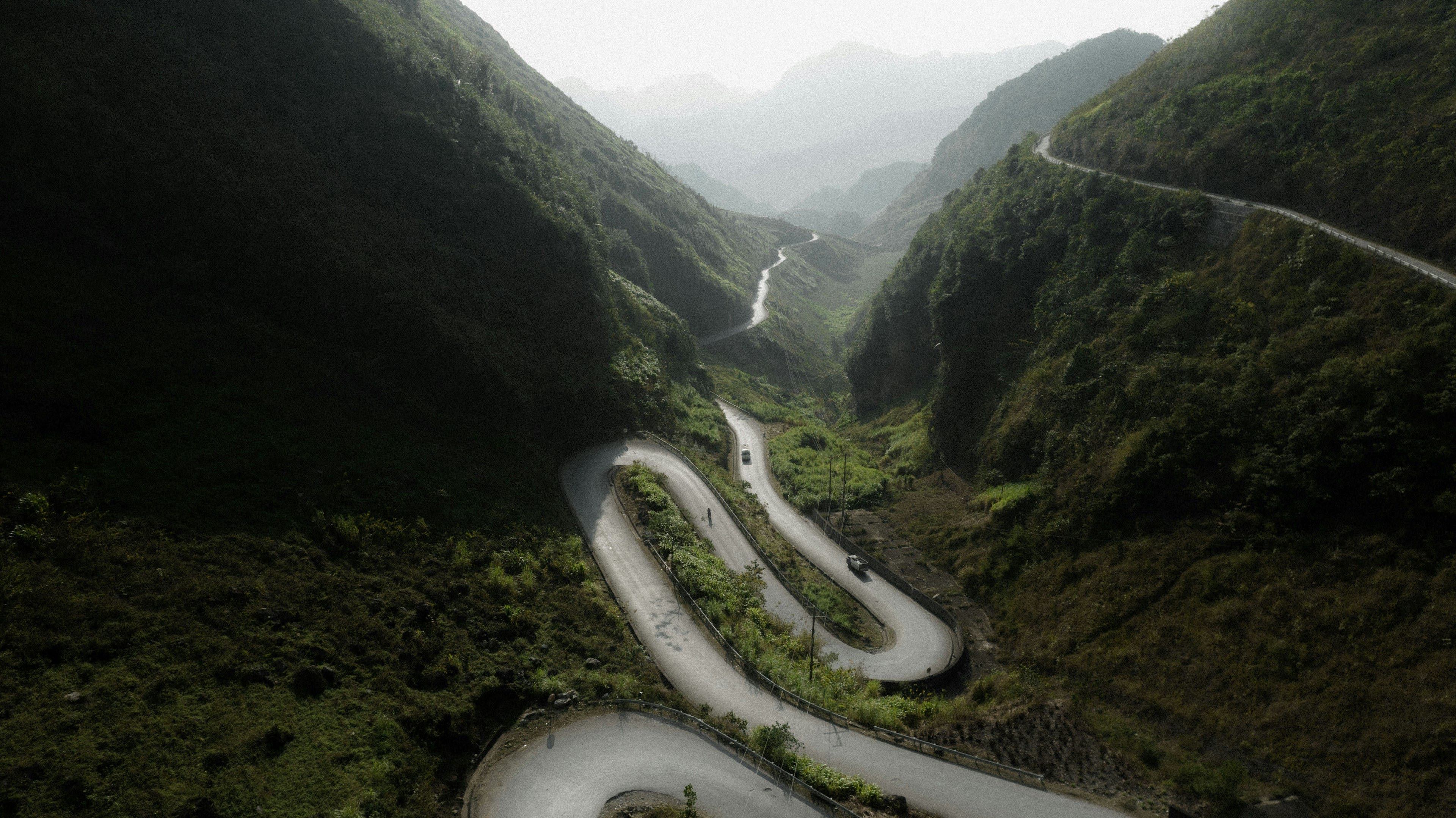 An aerial view of a road threading a deep green canyon
