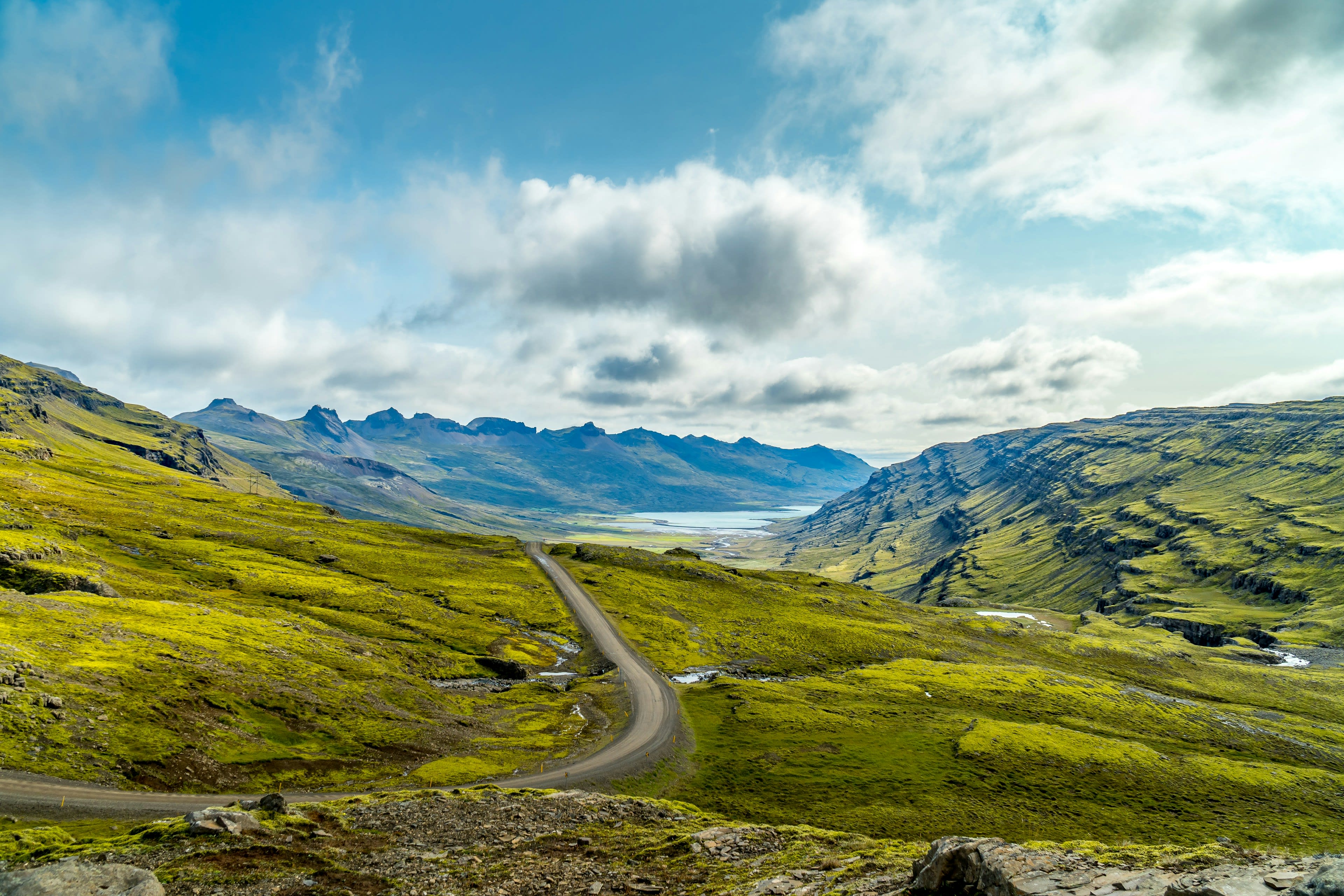 A gravel highland road winding between green mountains under moving cloud