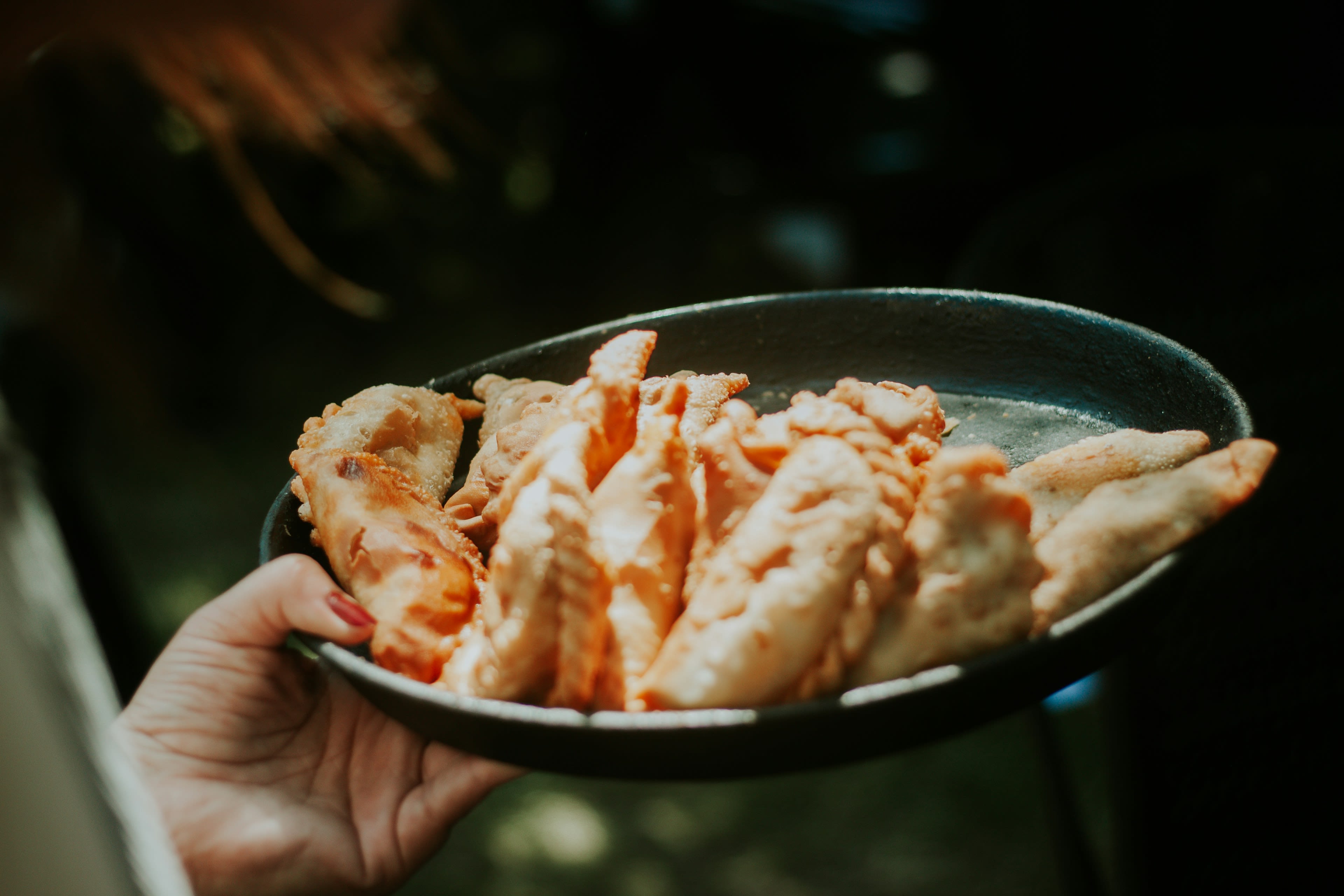 A hand holding a dark plate stacked with folded pastry empanadas