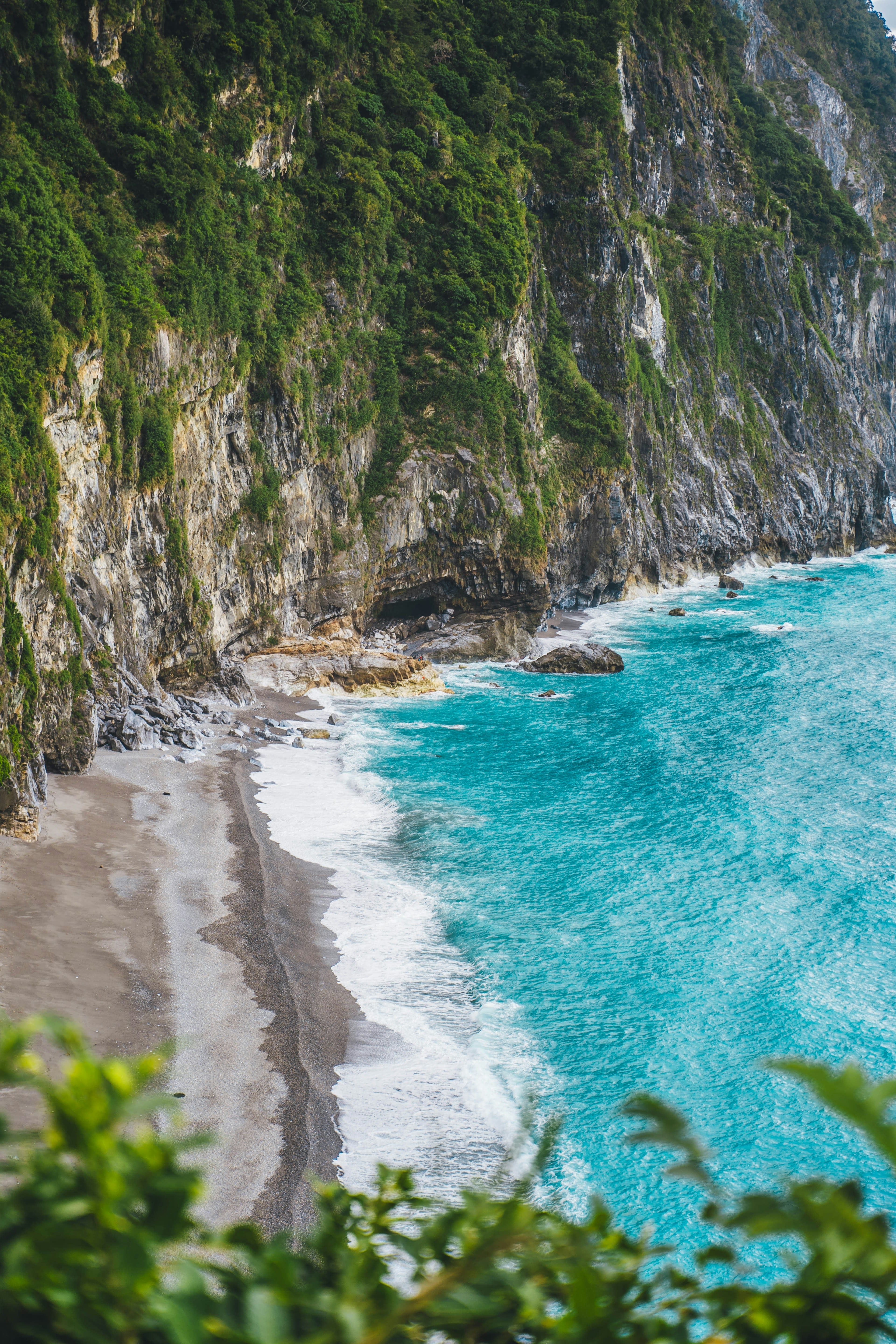 A steep green cliff dropping into a deep blue sea with a small beach below