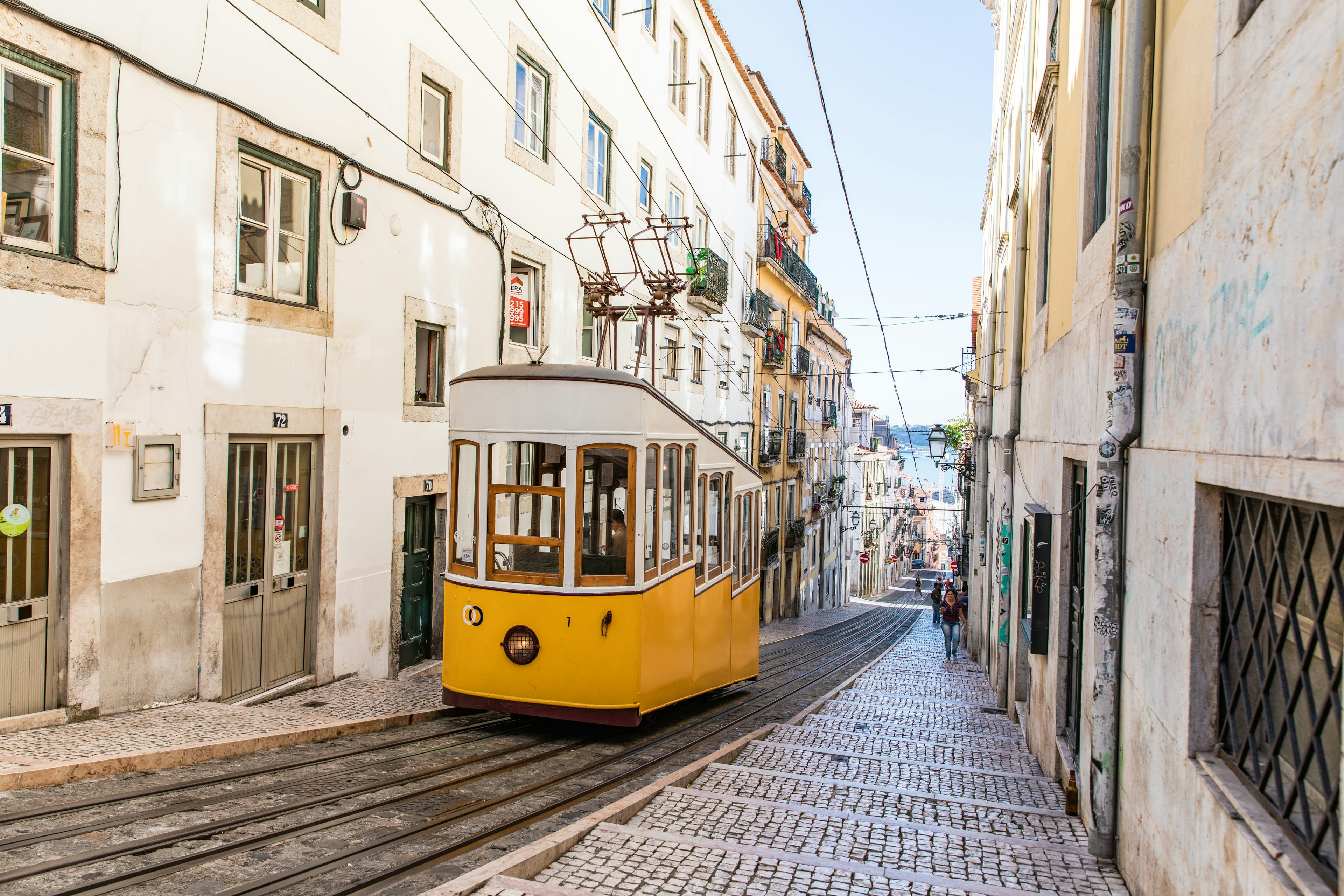 A yellow tram passing through an extremely narrow cobbled street between old buildings